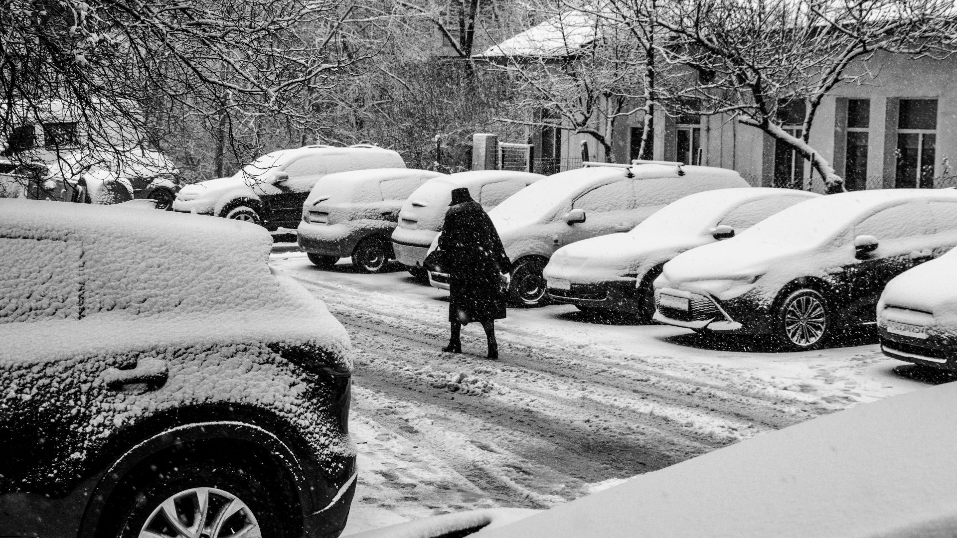 A lone person walks through a snow-covered parking lot during a winter storm.