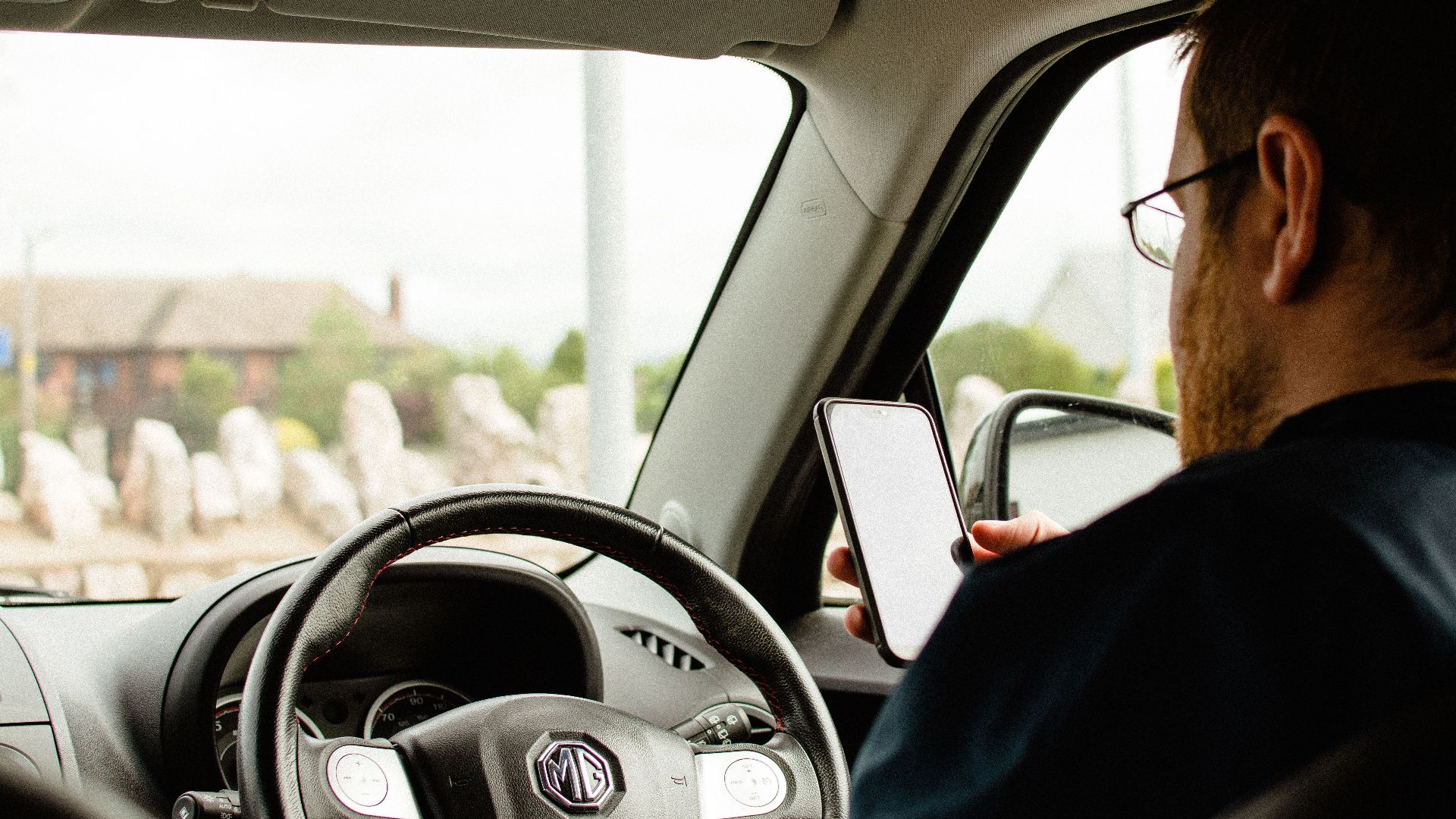Back view of anonymous male in casual clothes sitting in car behind wheel and using smartphone