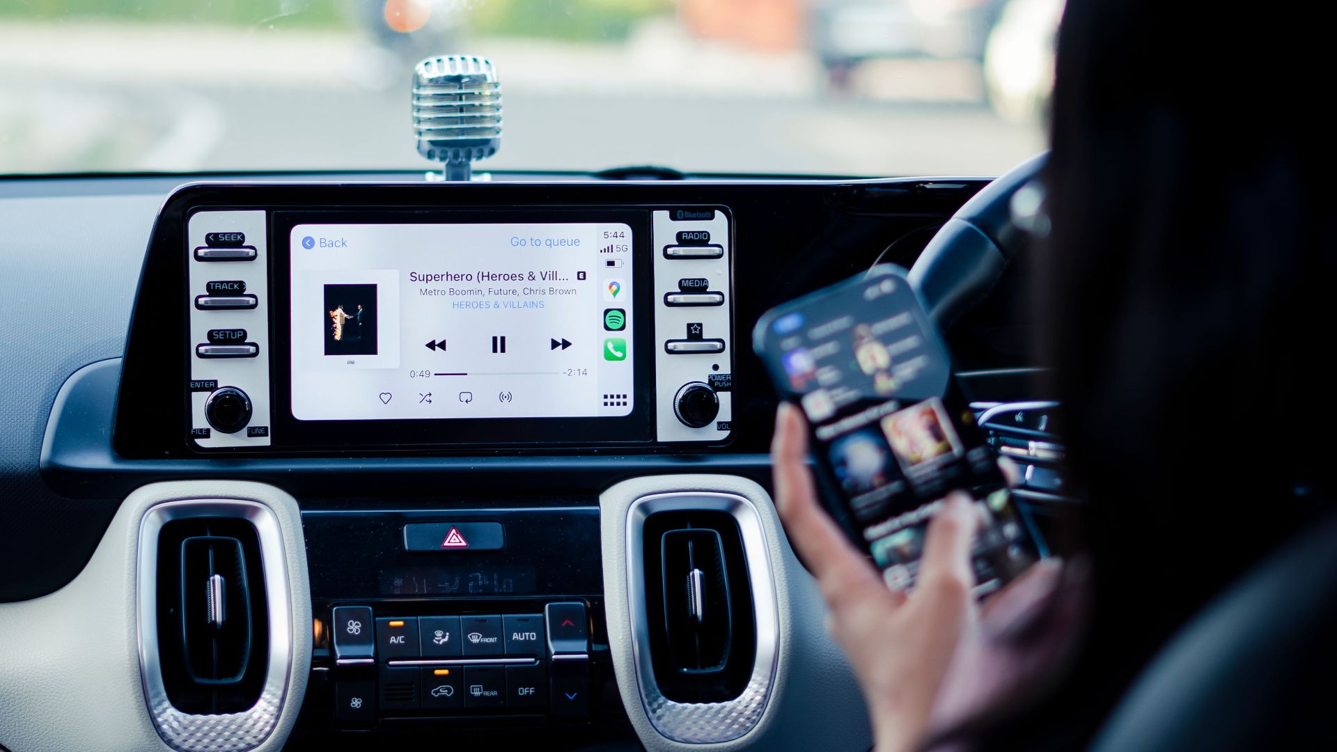 Car dashboard with a touchscreen display and person using a smartphone inside a vehicle.