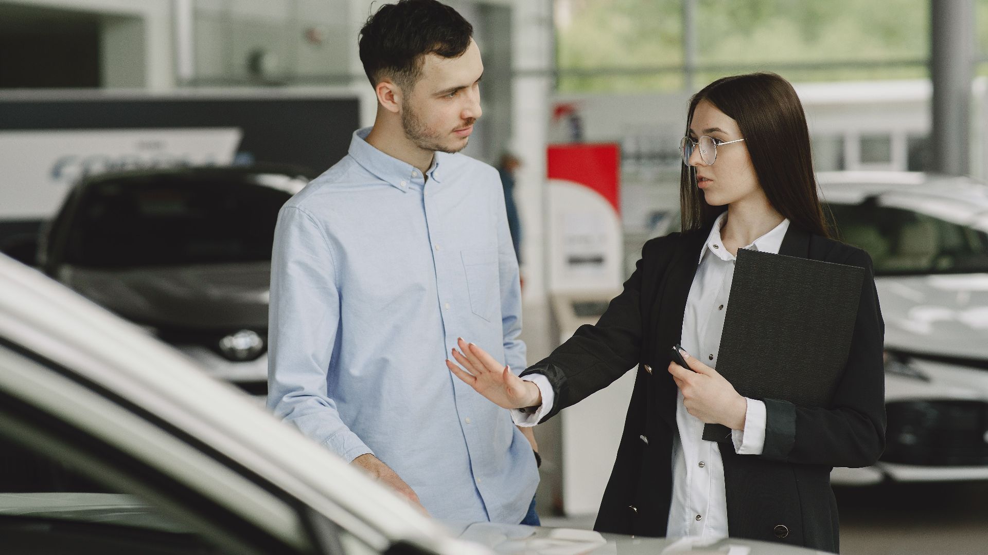 A salesperson and customer discussing car features in a dealership setting.