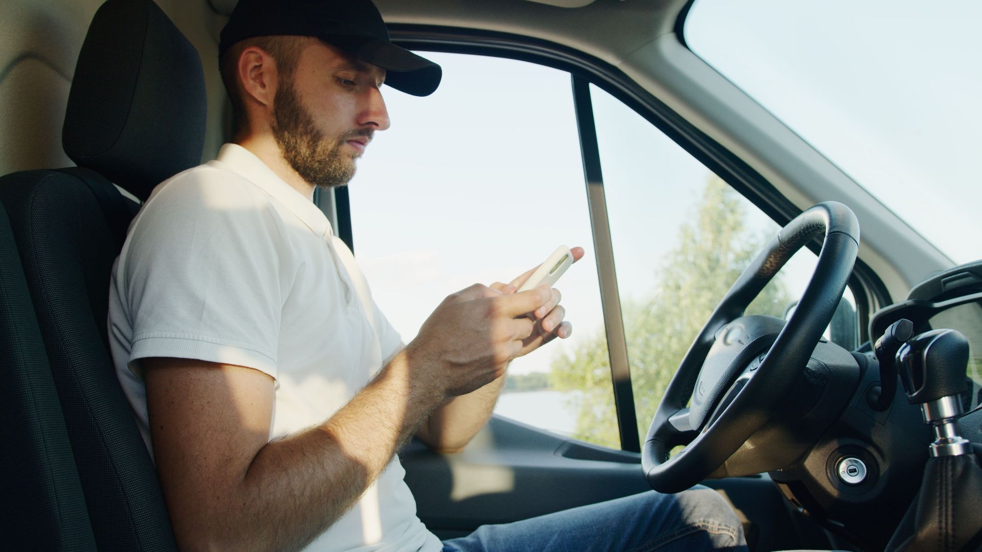 Side view of a man using a smartphone in a parked vehicle on a sunny day.