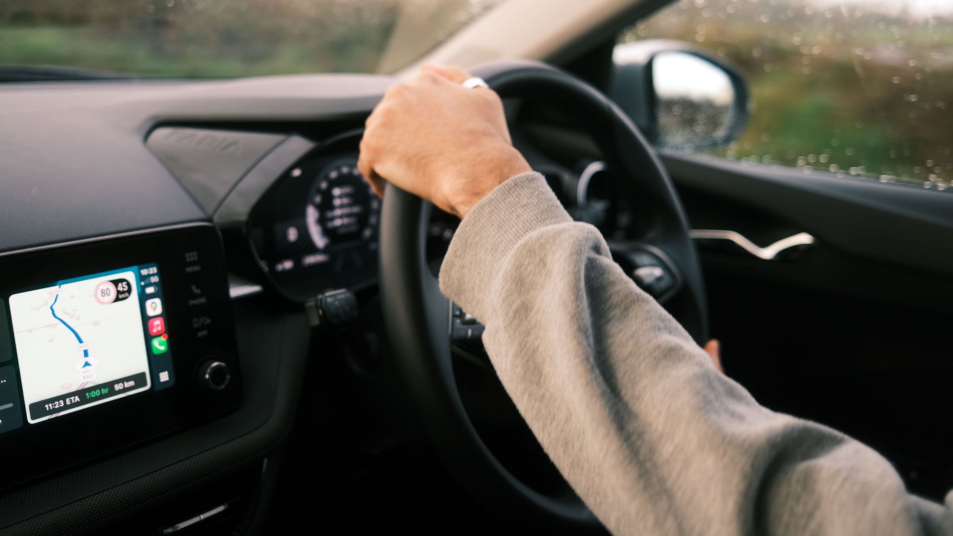 A person drives through rainy conditions, guided by GPS technology on their dashboard.