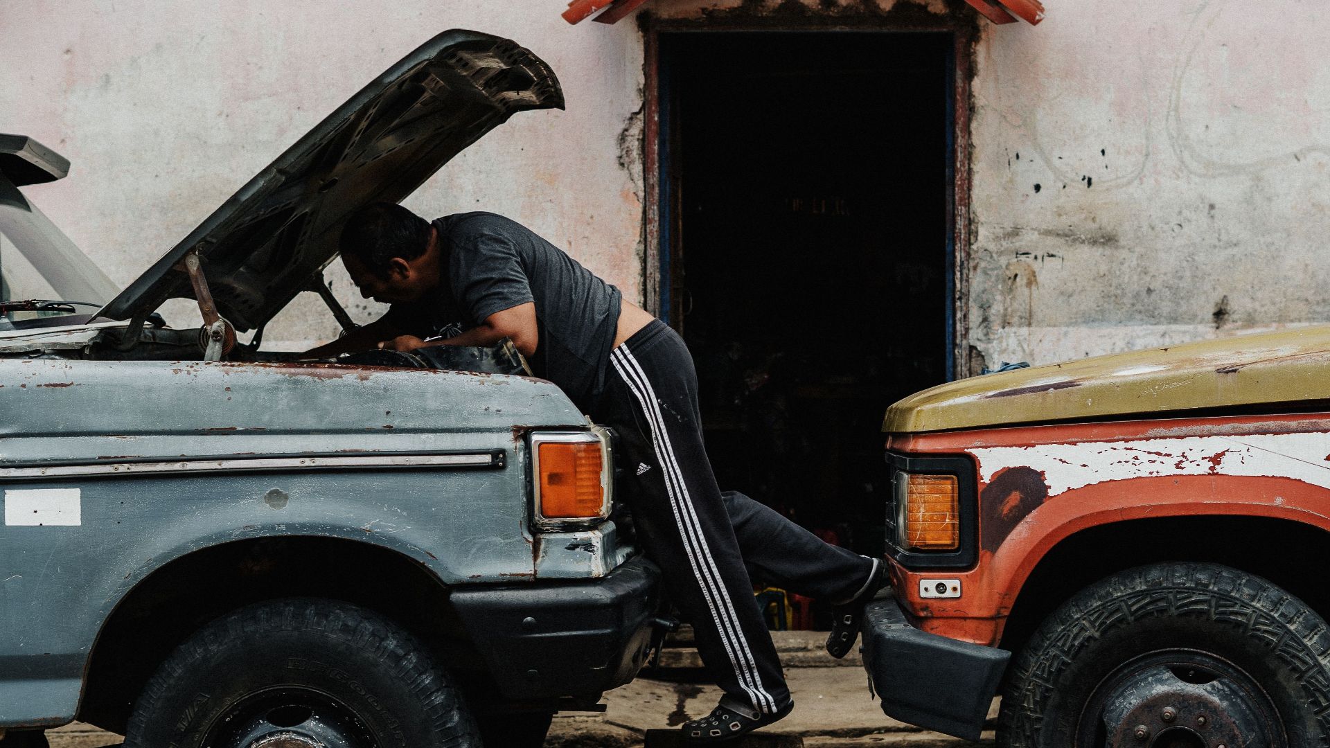 Mechanic working on vintage trucks in an urban setting, highlighting a candid street scene.