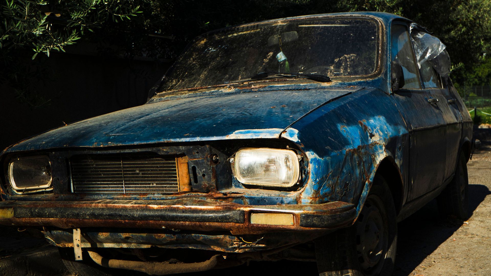 A rusty, classic car sits abandoned on a sunny street, showcasing nostalgic decay.