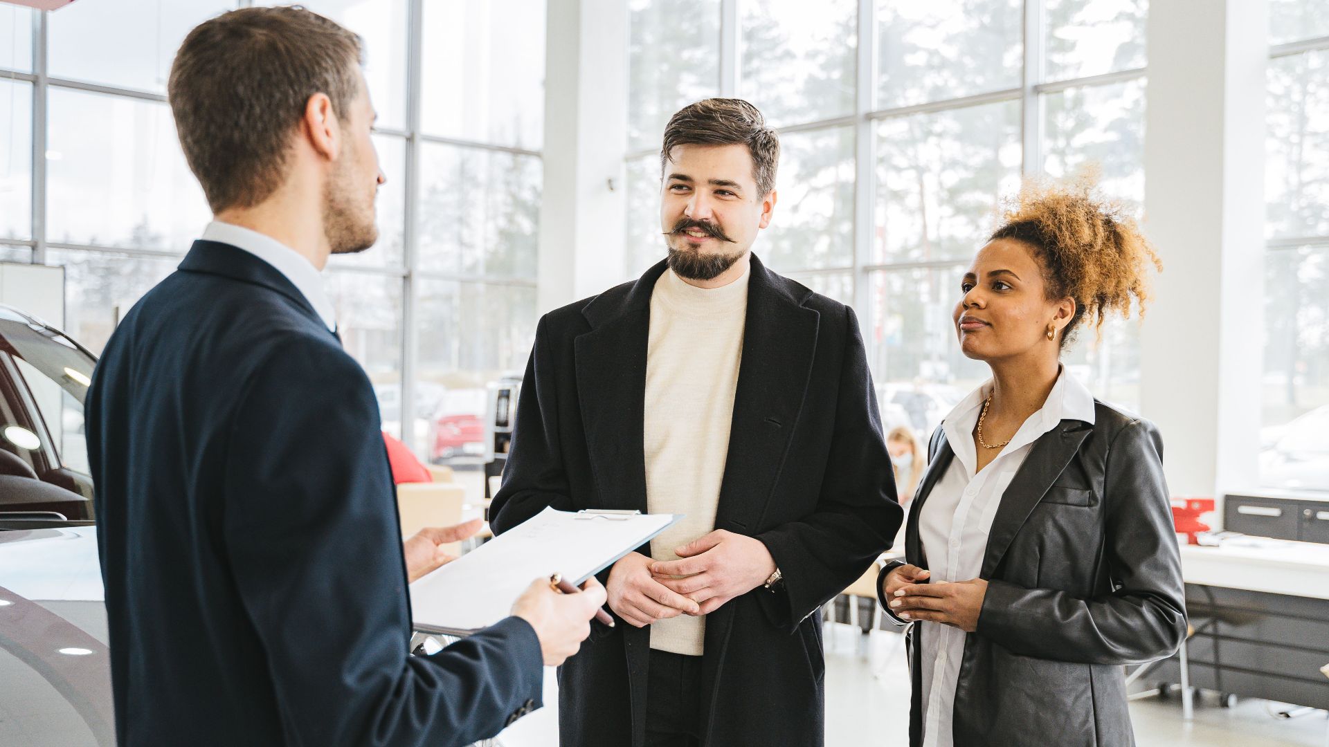 Happy couple discussing car purchase with dealer in showroom. Professional interaction and consultation.