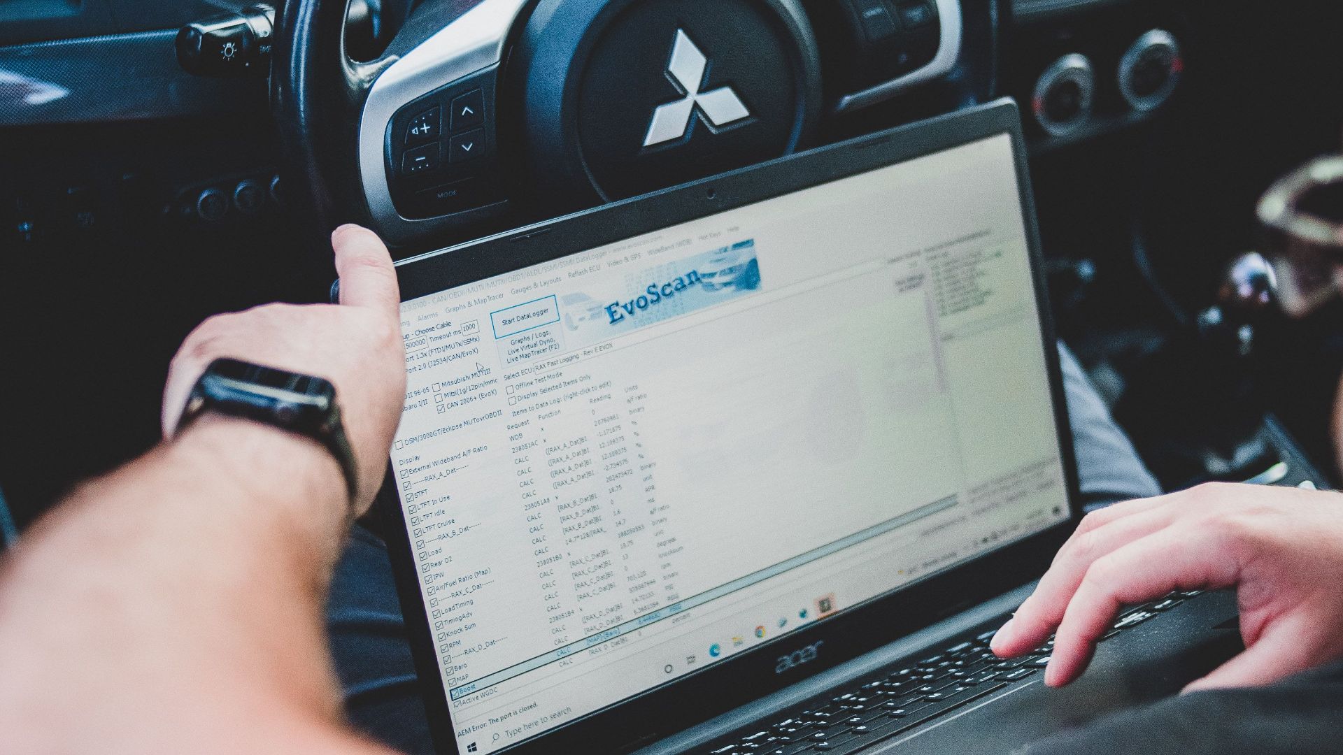 A person using a laptop inside a car for vehicle diagnostics, showcasing technology integration in automotive settings.