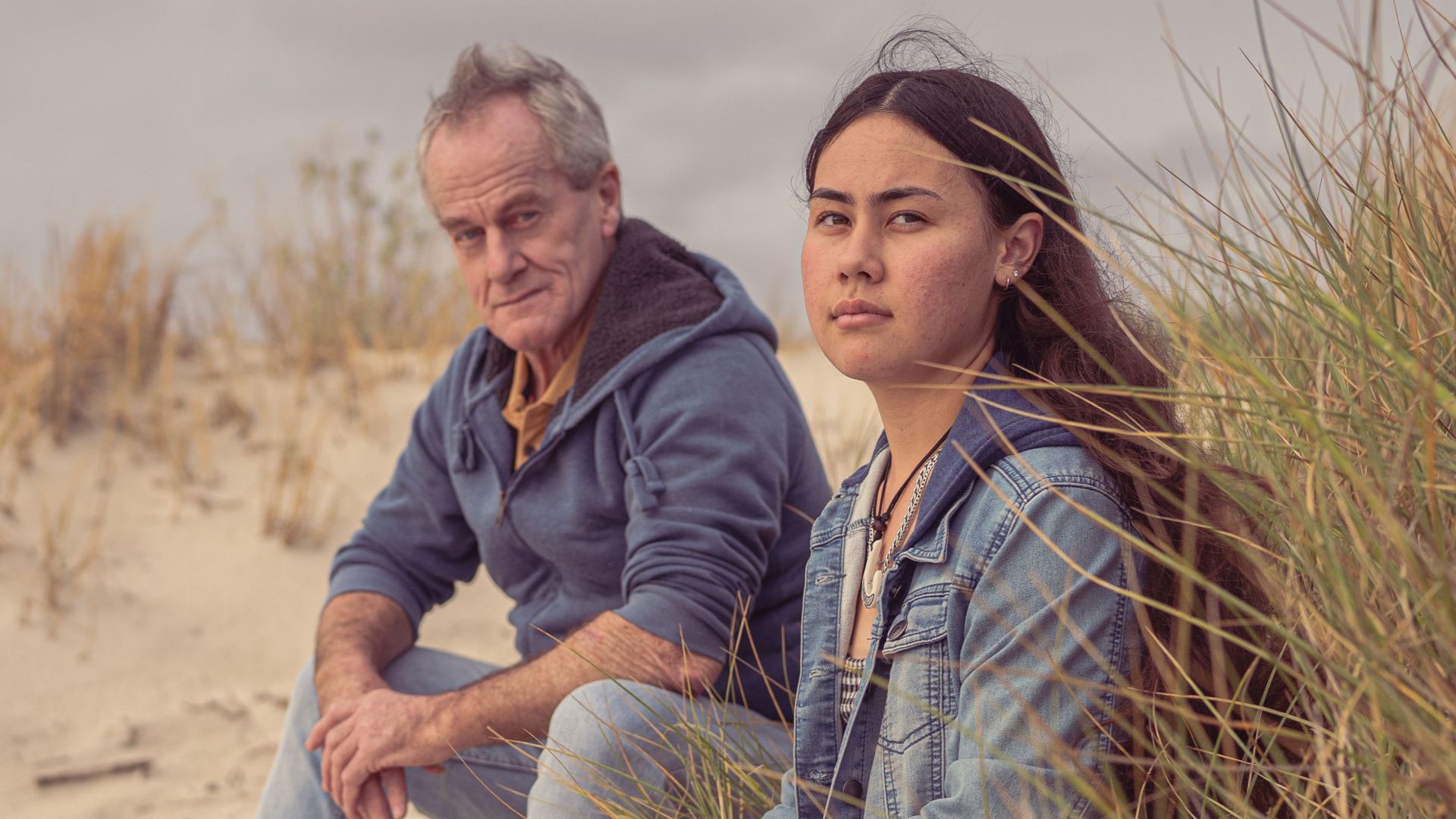 Elderly man and teenage girl sitting on a sandy beach, enjoying a relaxing day by the shore.