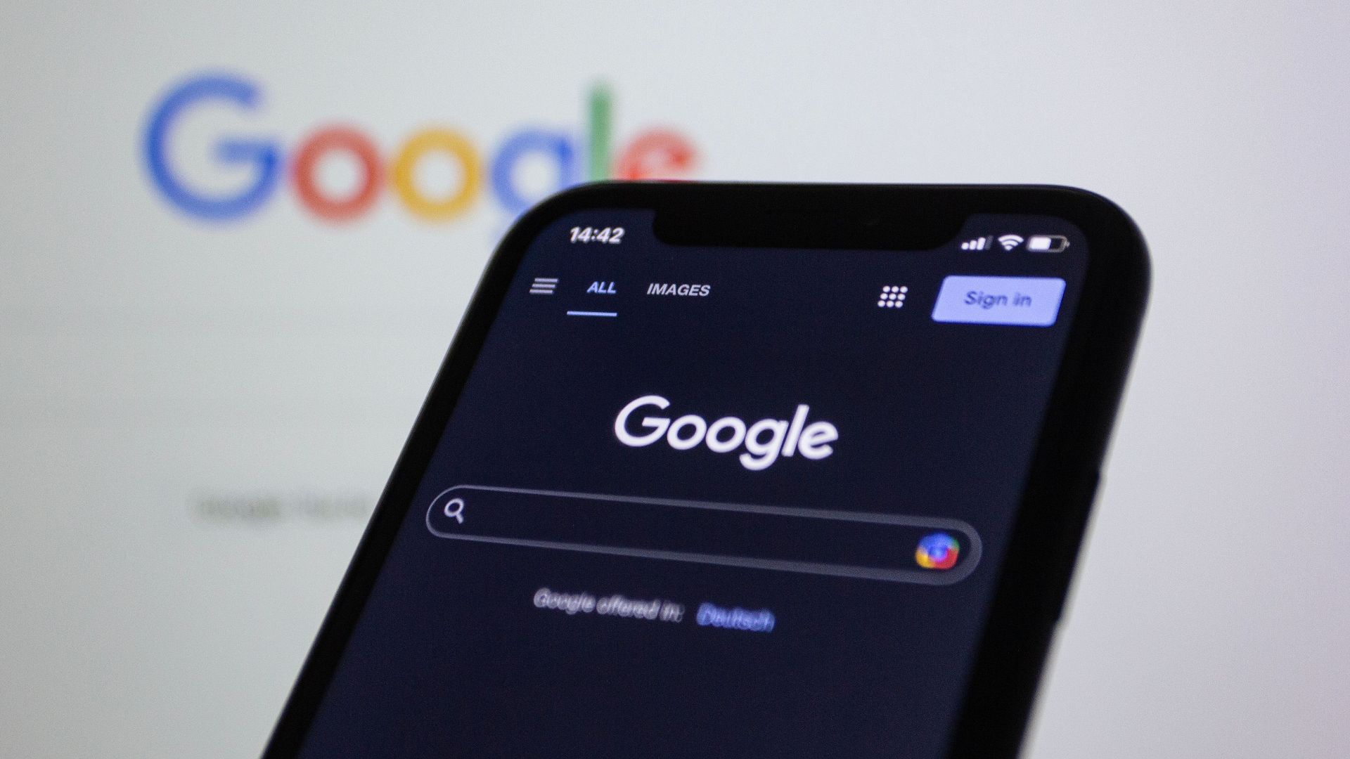 Smartphone screen showing Google search in dark mode with the Google logo in the background.