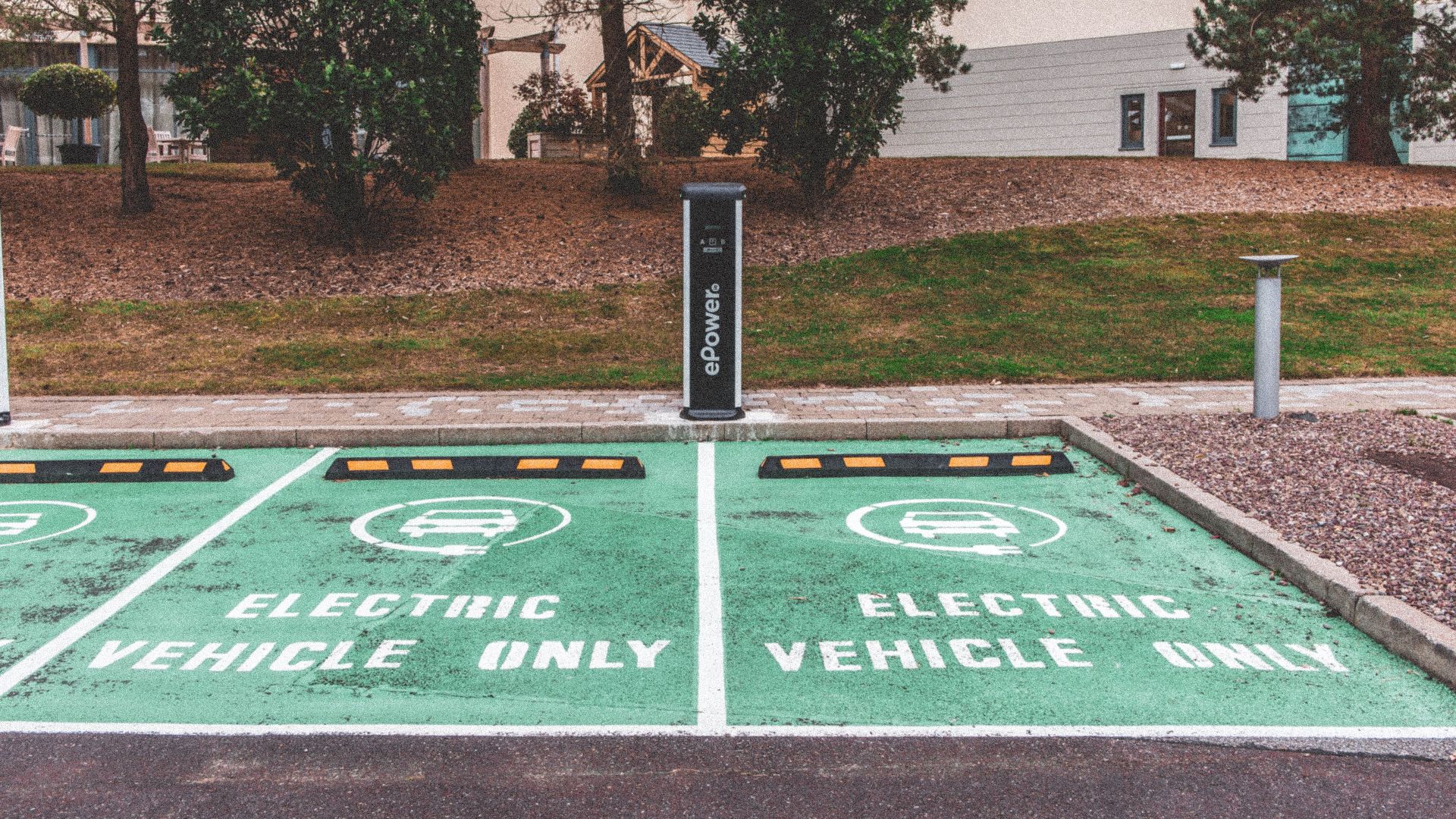 Green electric vehicle parking with charging station in urban environment.