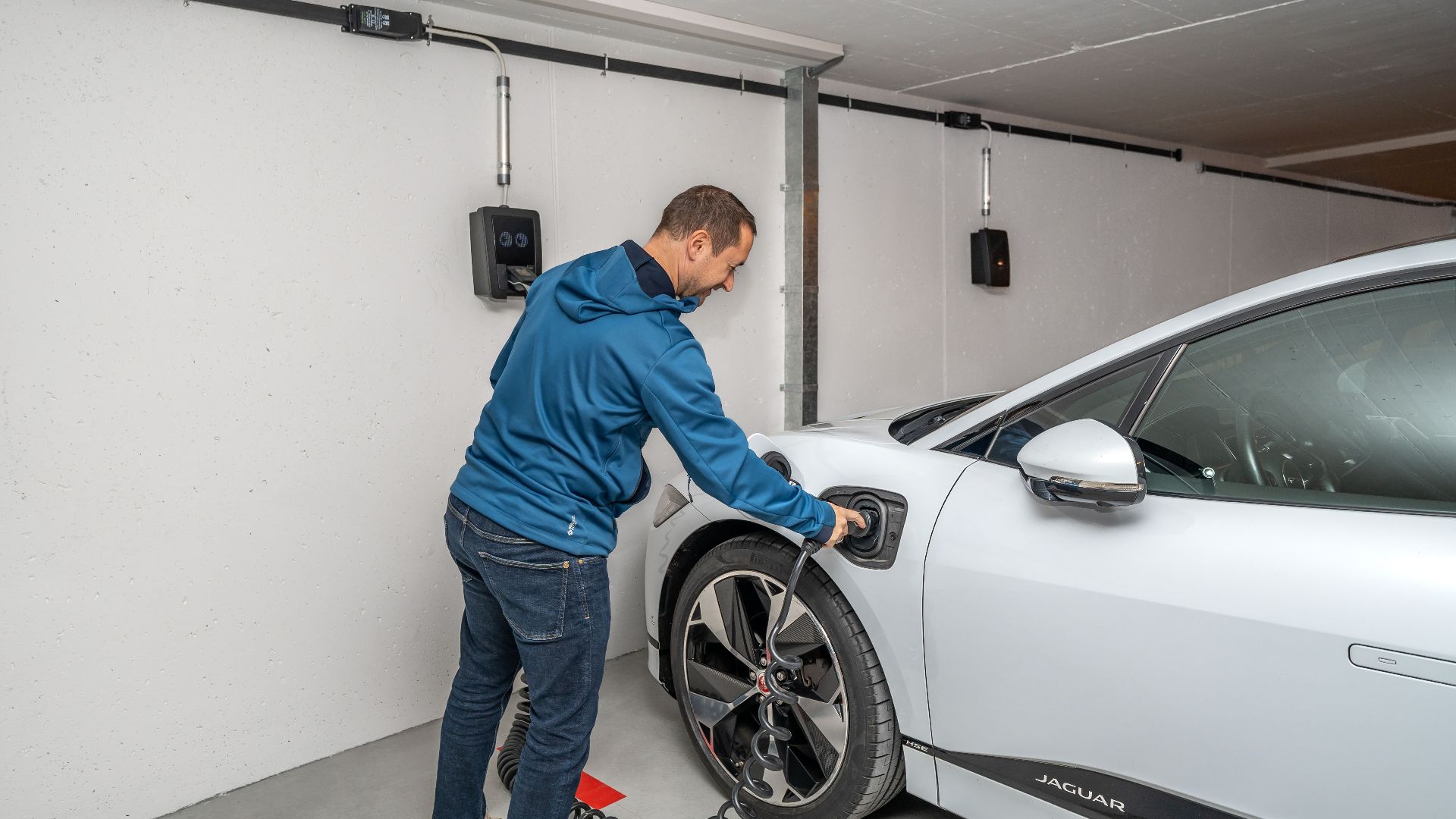 A man connects an electric car to a charging station in a modern indoor garage setting.