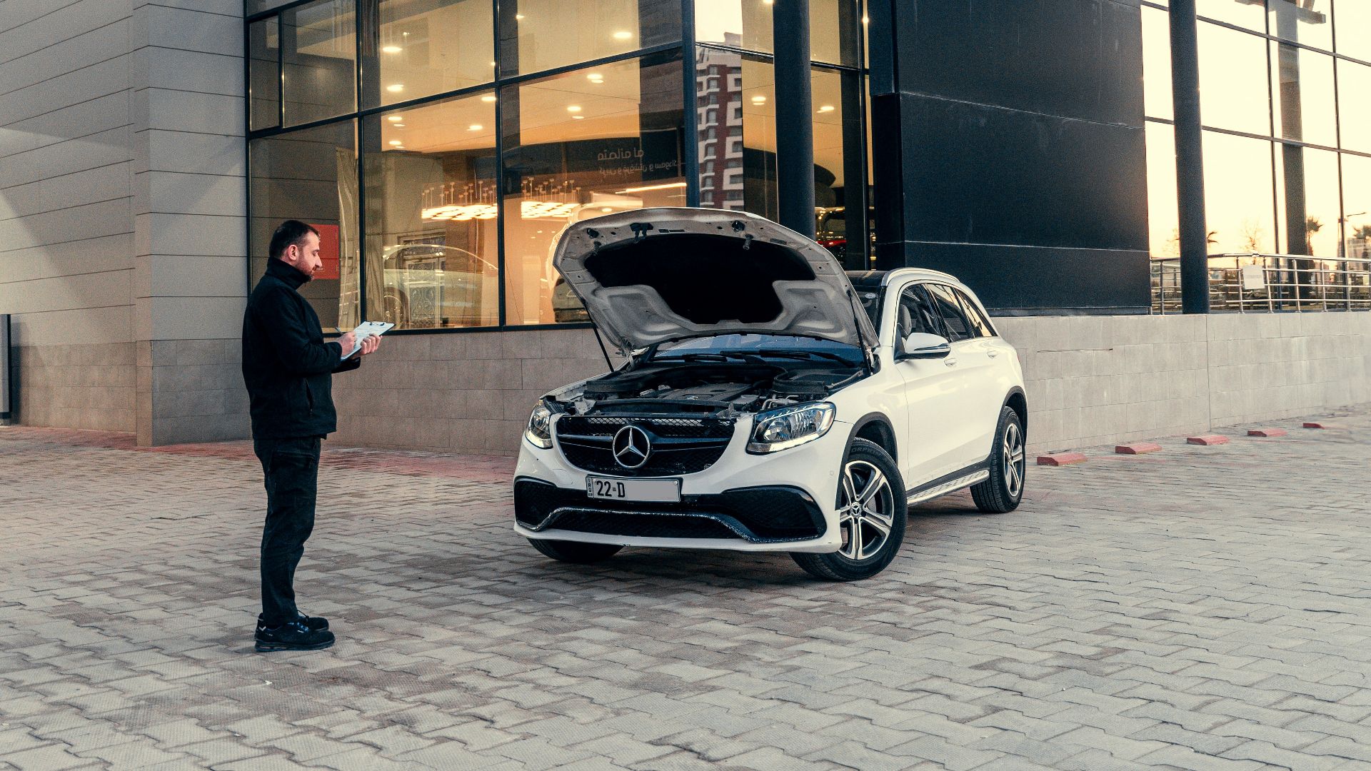 Man looking at car with hood open outside dealership