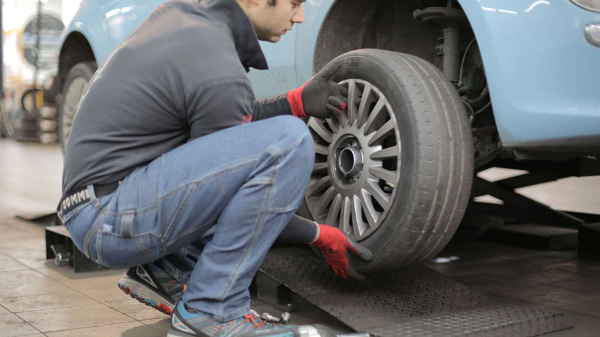 Mechanic changing a car tire indoors, using tools for vehicle maintenance.
