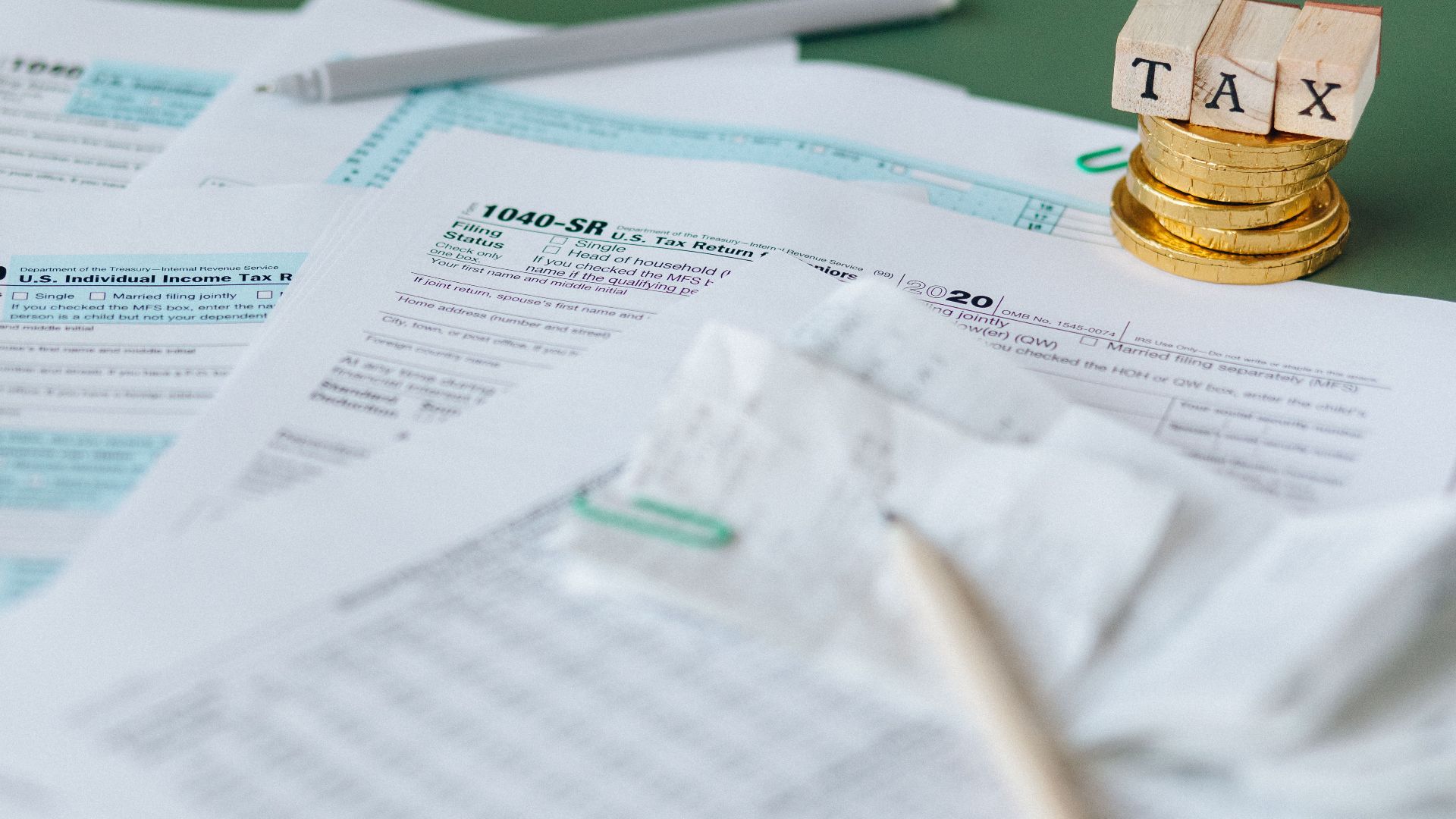 Stack of tax forms and coins with a 'TAX' stamp, symbolizing finance and accounting.