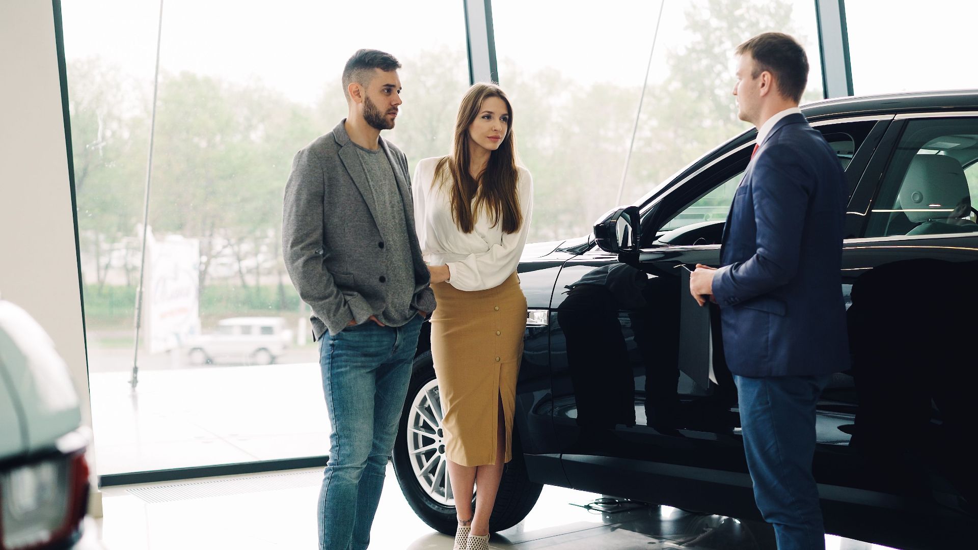 A couple converses with a salesperson about buying a car inside a dealership.