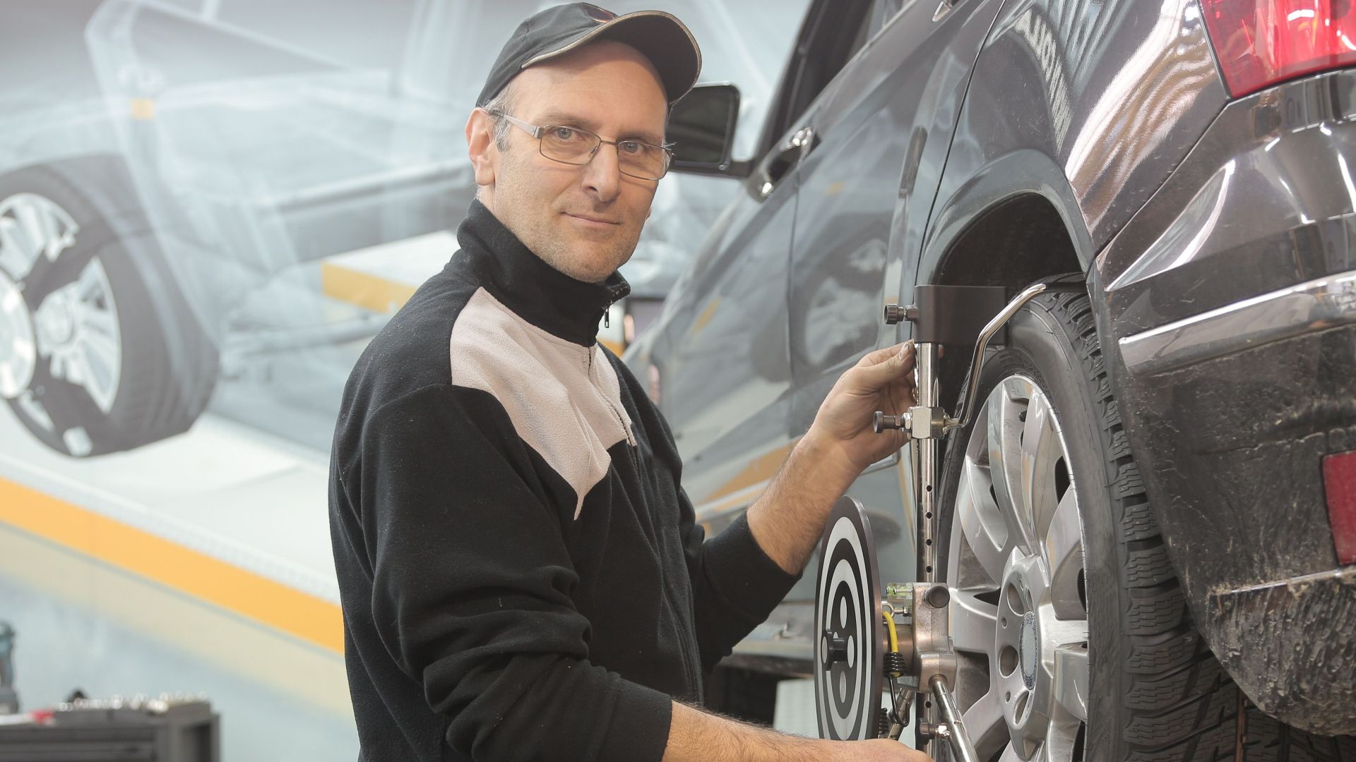 Mechanic performing wheel alignment on a car in a professional garage setting.