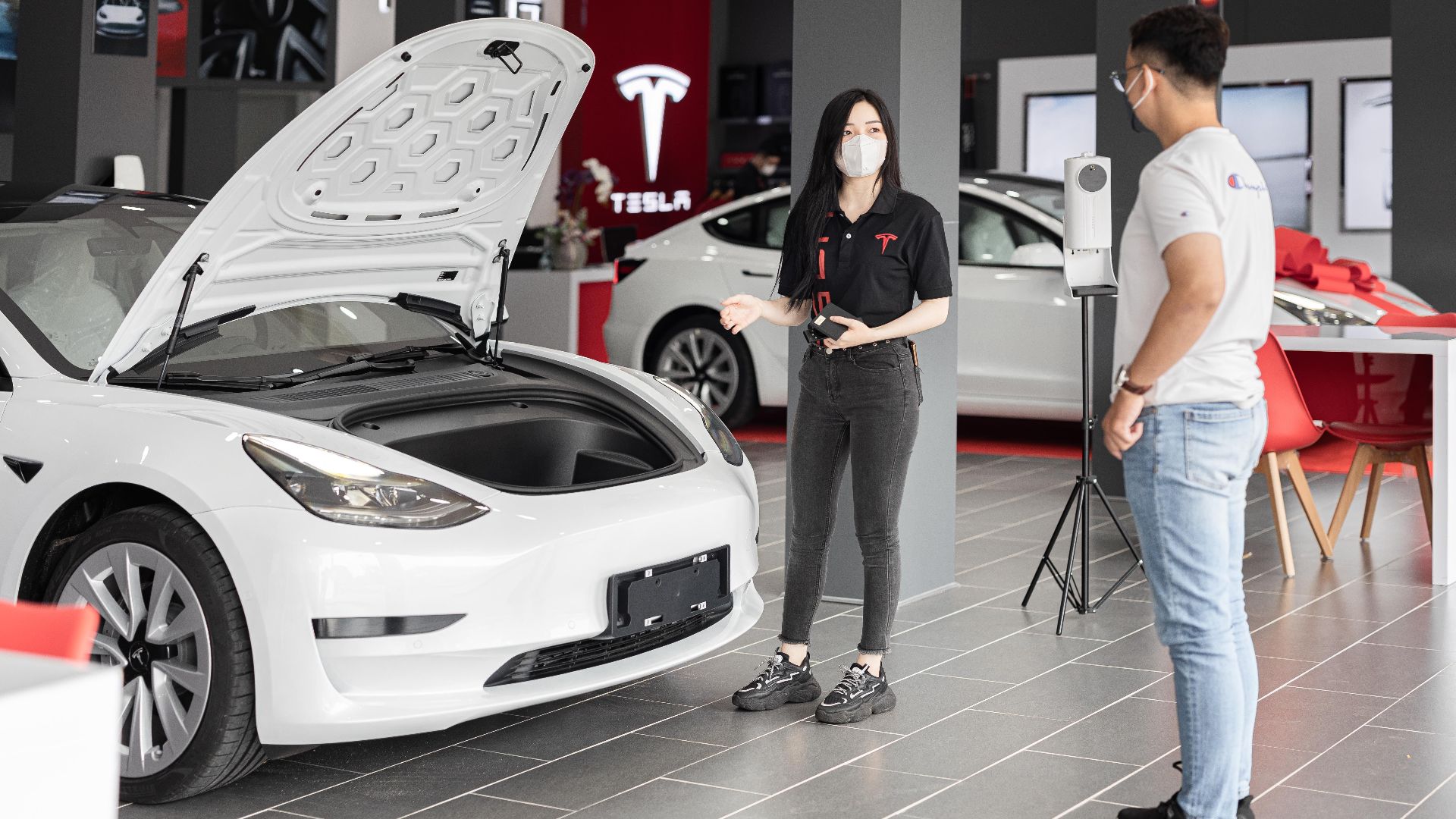 A customer talks with a sales representative about a Tesla Model 3 in a car dealership, showcasing the electric car's features.