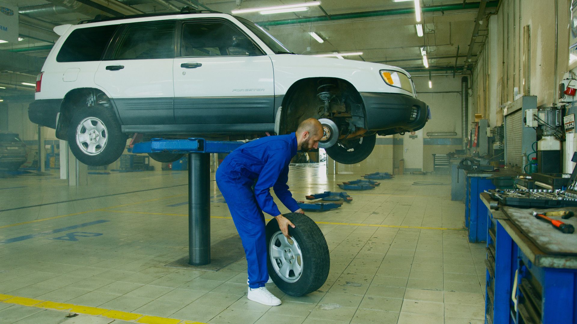Mechanic replacing a tire on a lifted SUV in a professional auto workshop.
