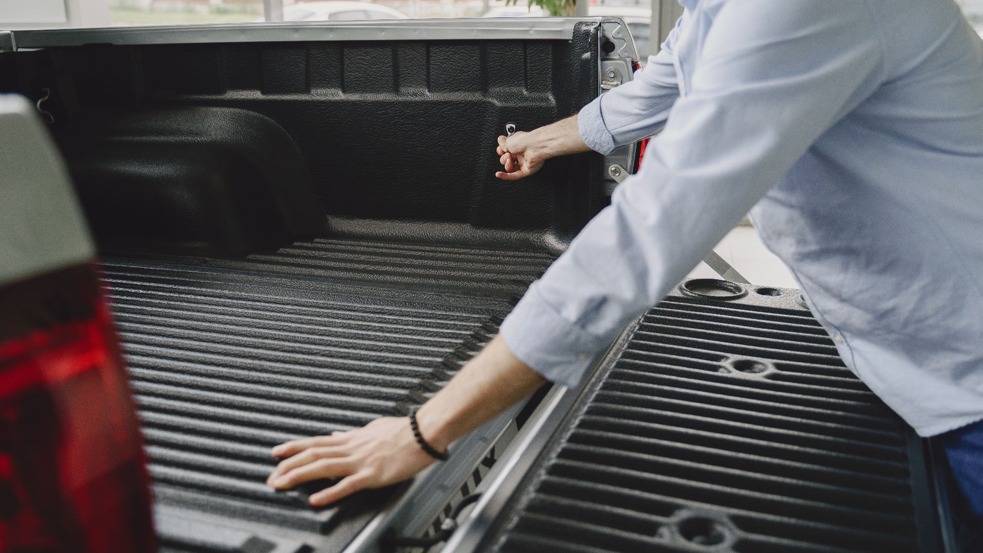 A man in a blue shirt opens the bed of a truck in a brightly lit indoor space.