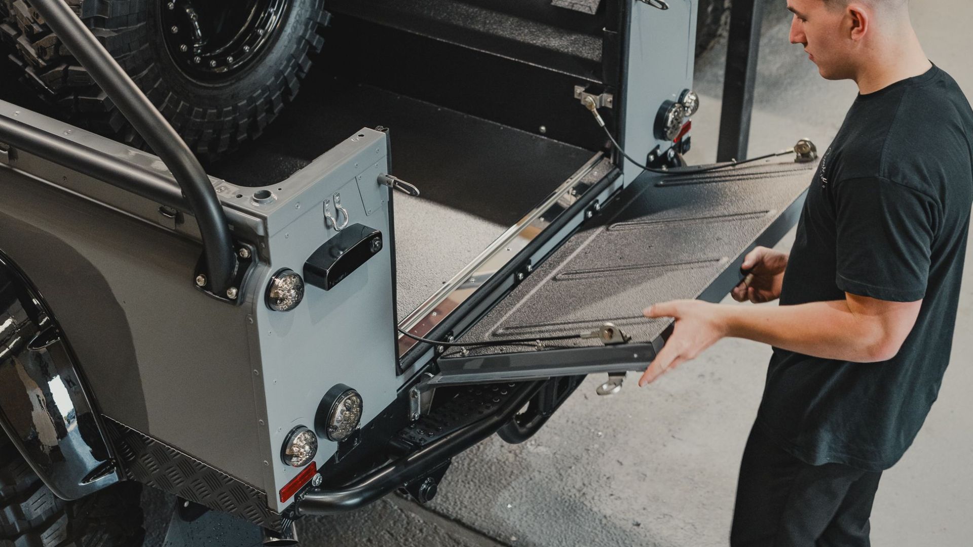 A man checks a rugged off-road vehicle with large tires in a vehicle workshop.