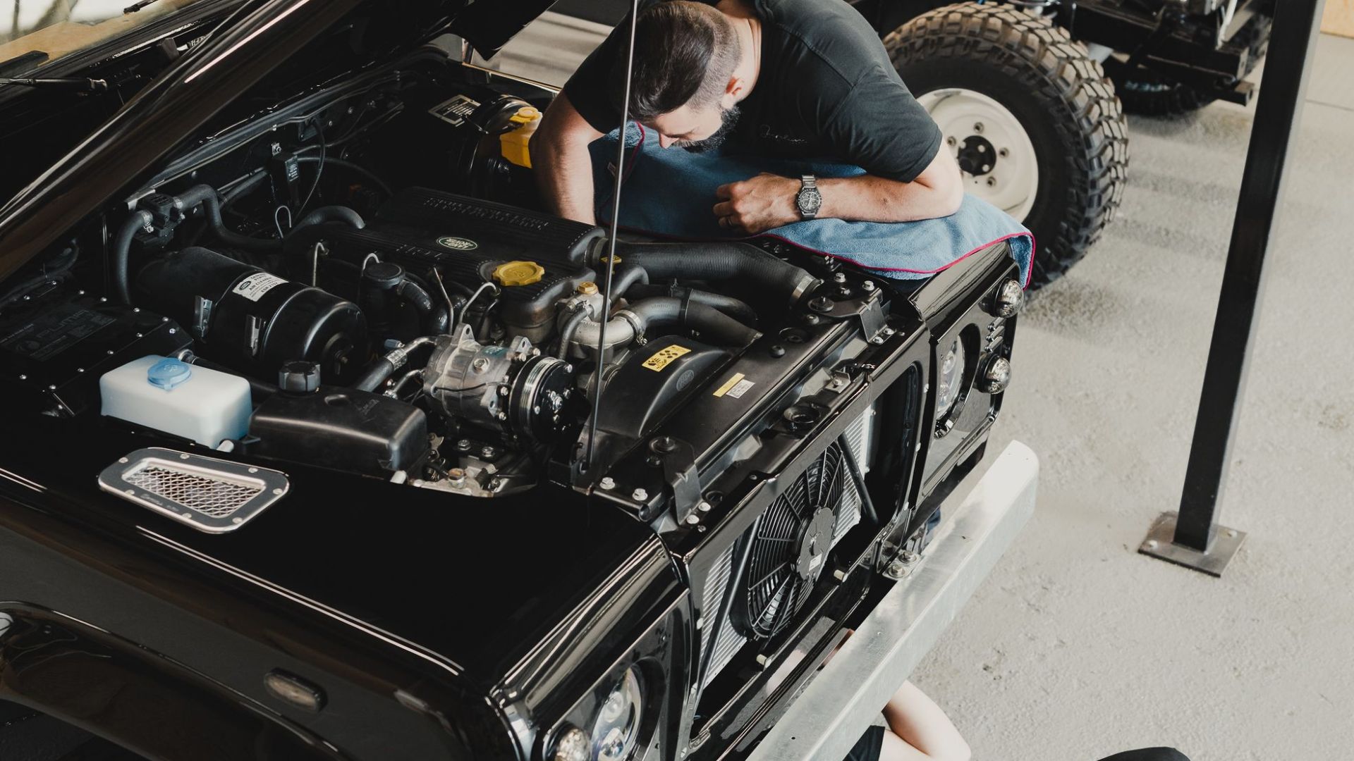 Two mechanics repairing a black off-road vehicle in a garage, focusing on engine work and maintenance.