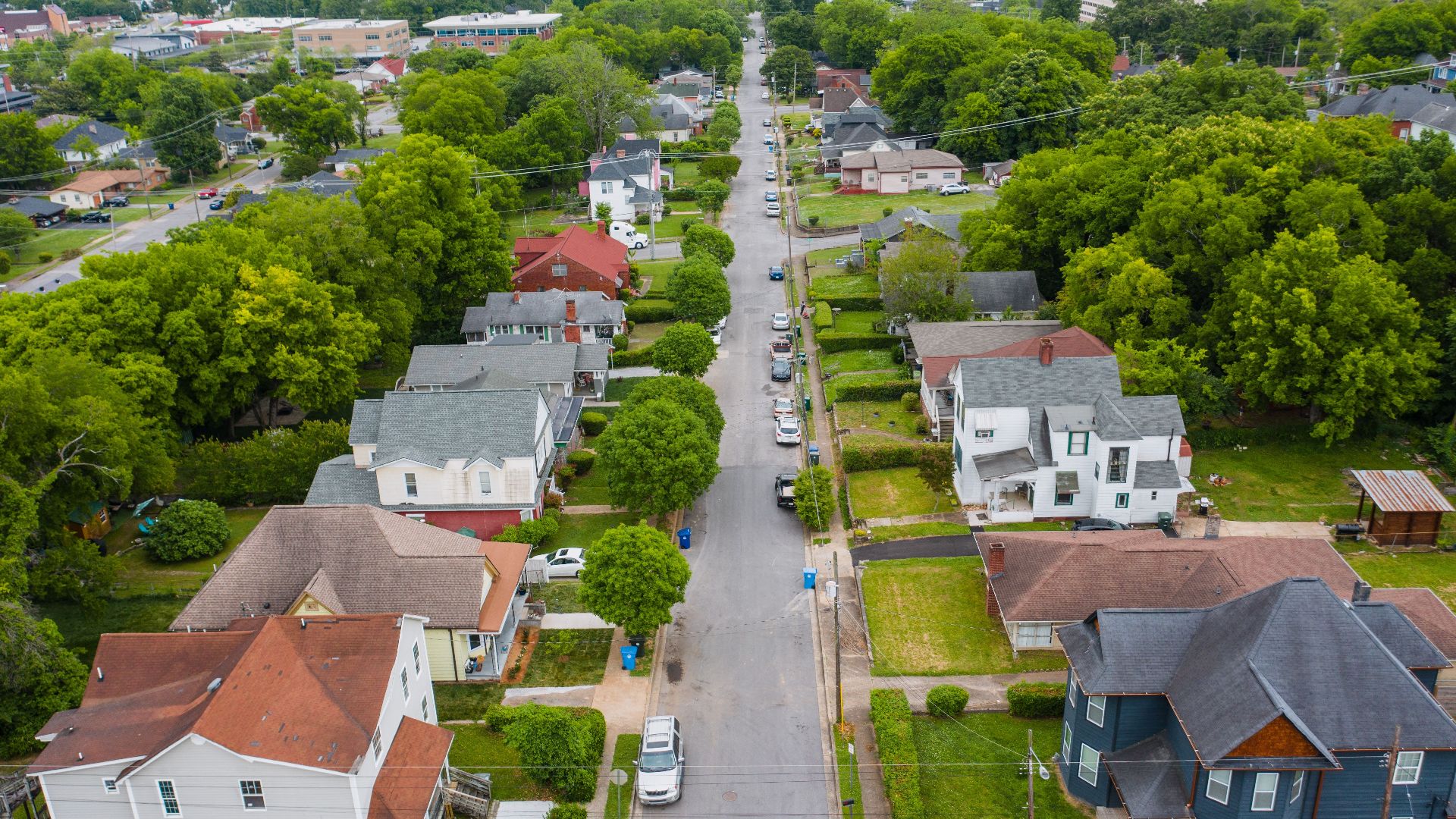 Drone shot showcasing a charming residential area with houses, trees, and parked vehicles.