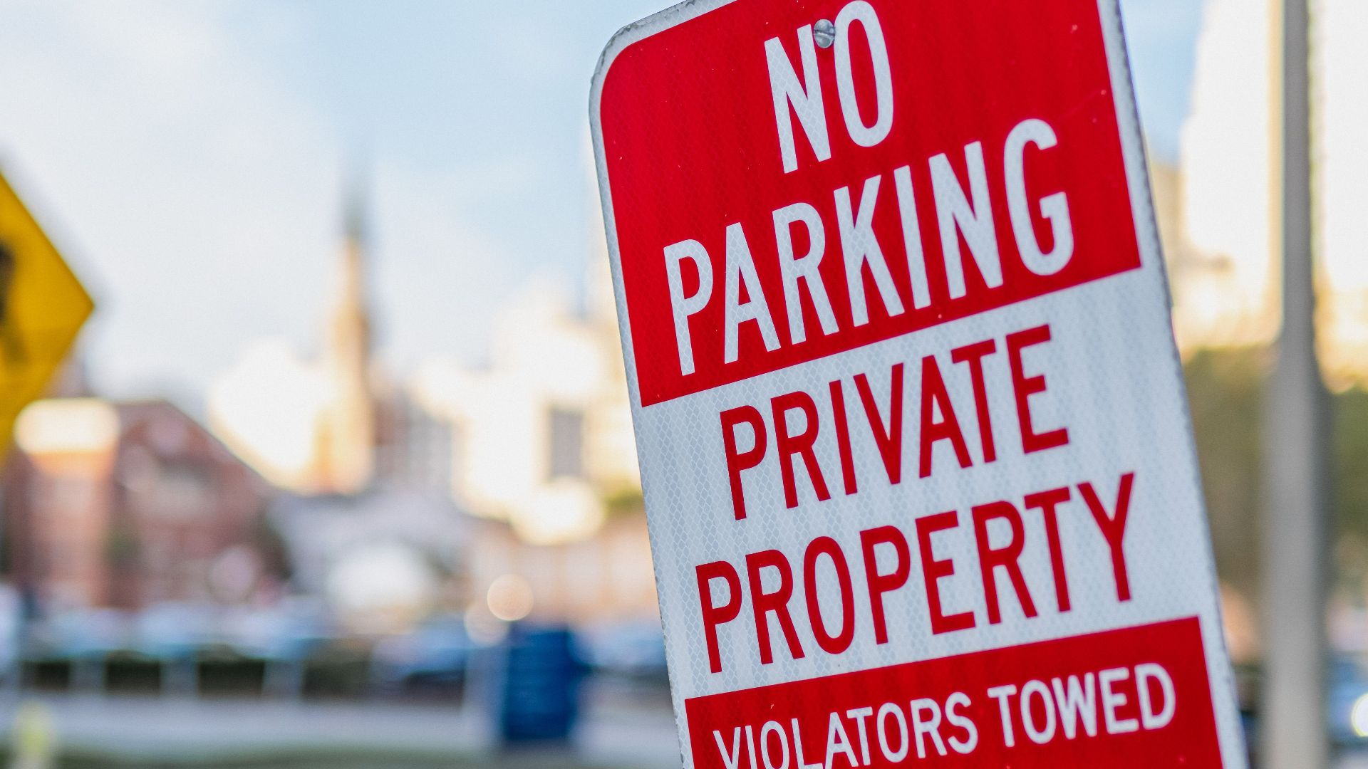 Red and white no parking sign on a private property warning of towing on a city street.
