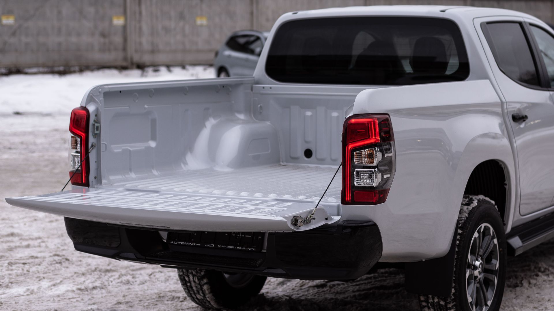 White pickup truck parked in a snowy industrial area, showcasing its open cargo bed.