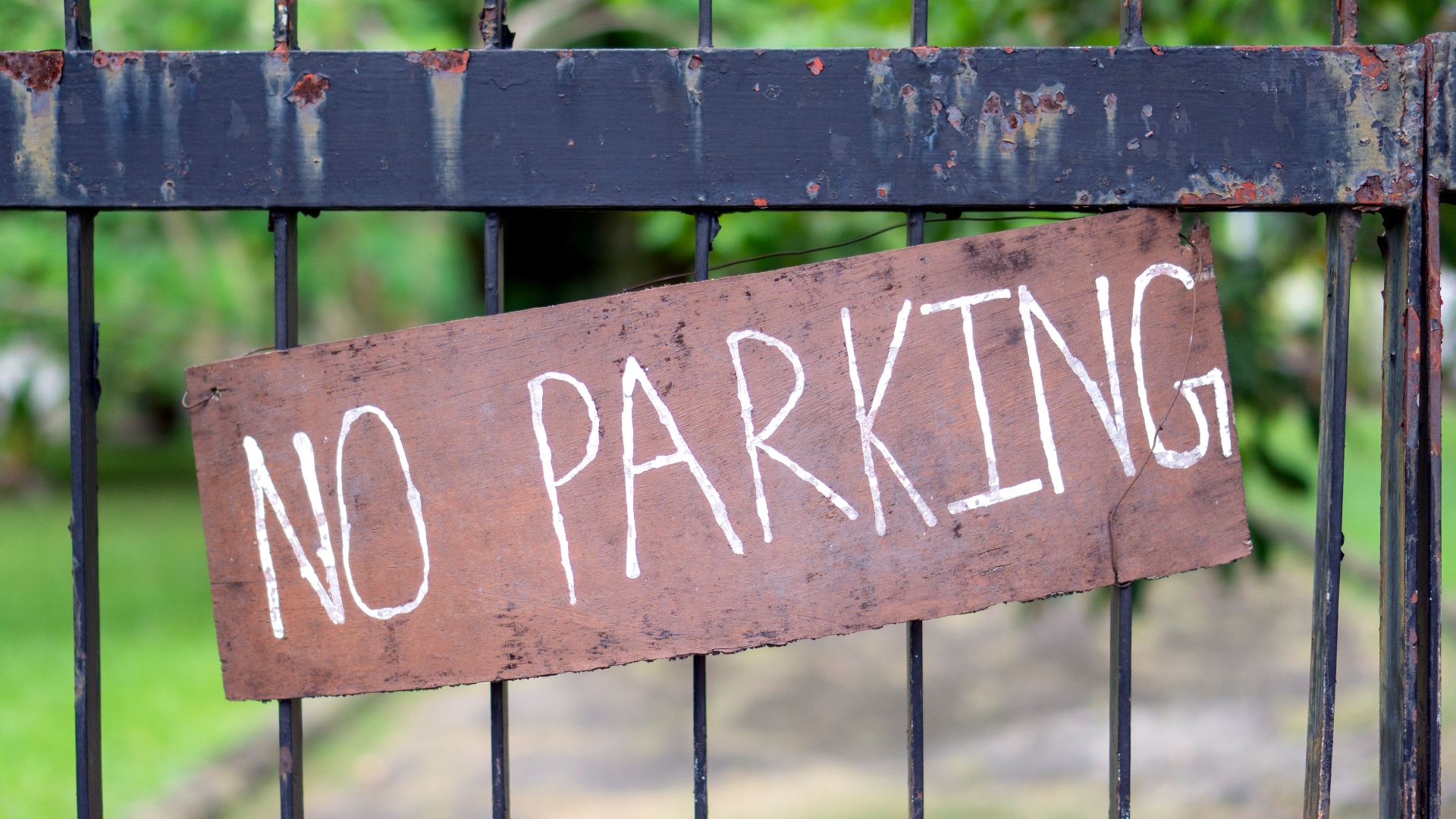 Close-up of a rustic 'No Parking' sign on a metal gate outdoors.