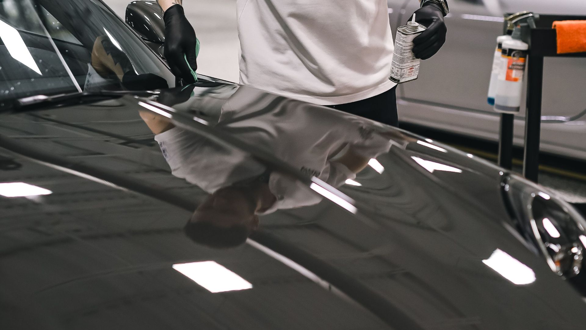 A dedicated employee expertly detailing a car hood in a clean, modern garage setting.