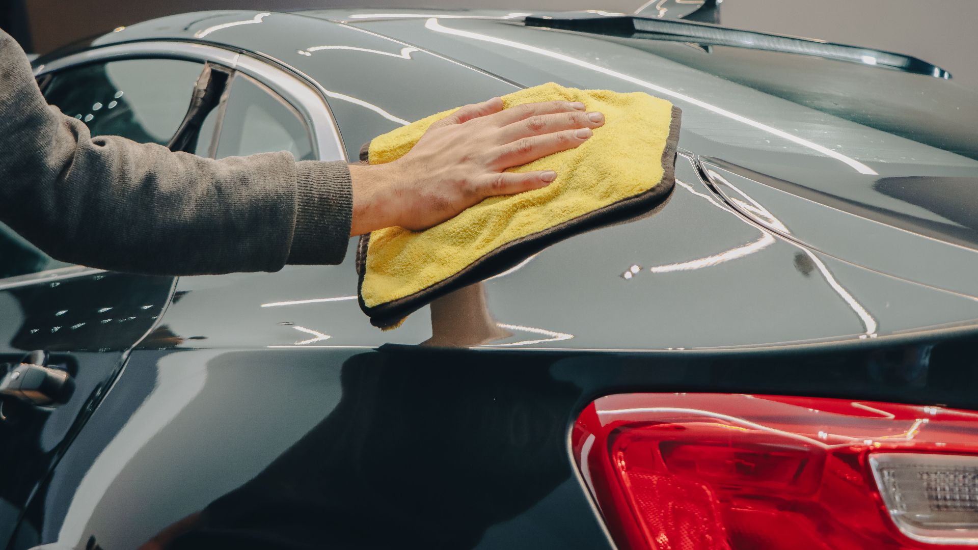 Close-up of hand polishing a shiny car with a yellow cloth indoors.