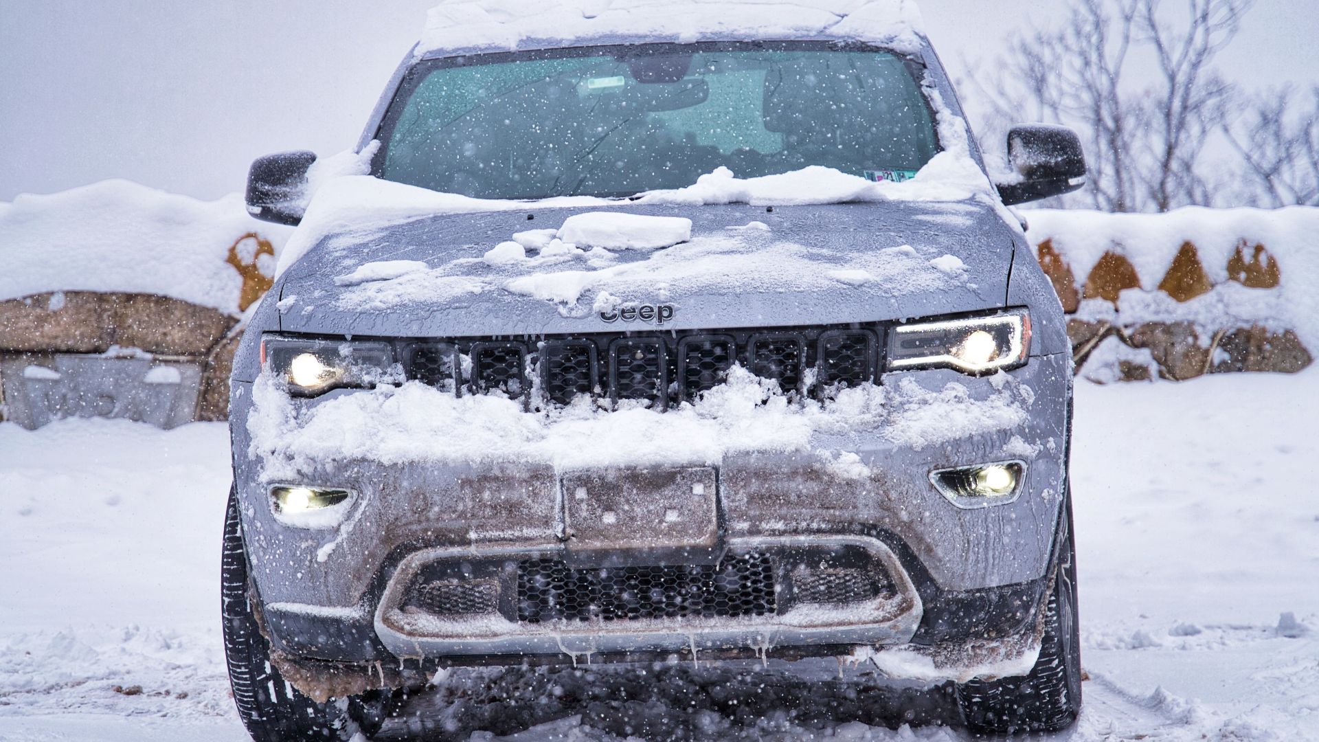 Front view of a Jeep covered in snow, parked outdoors during winter.