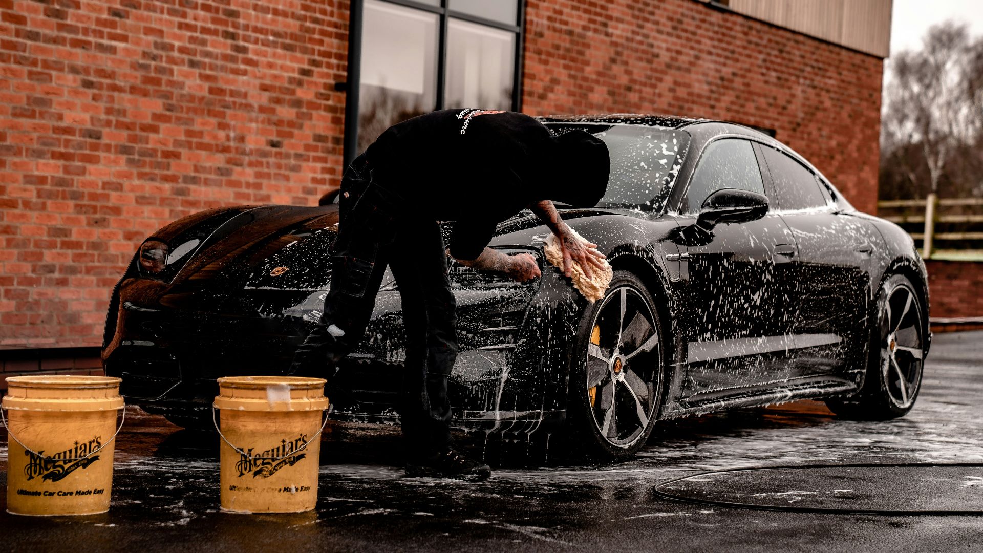 man in black jacket and pants leaning on black car