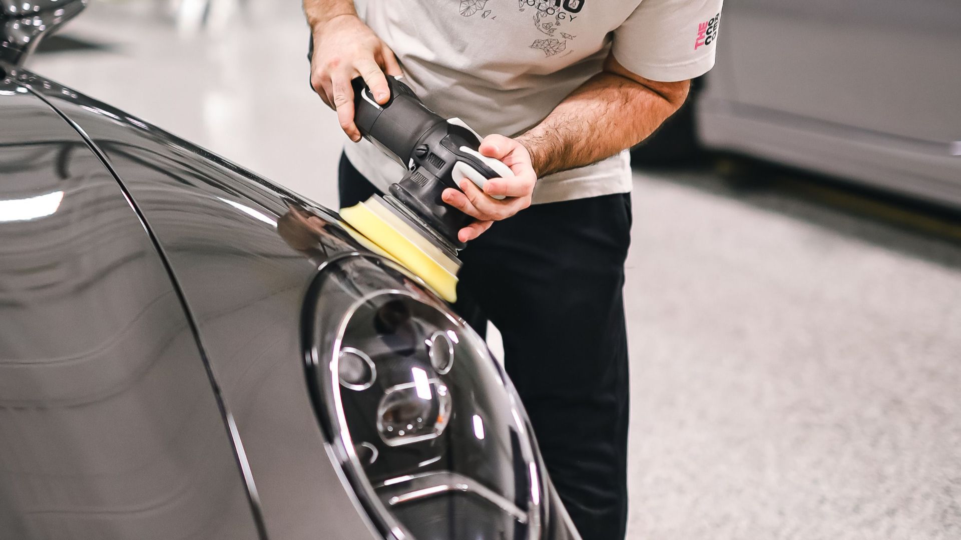 Man polishing a car's hood with precision in a modern automotive workshop.