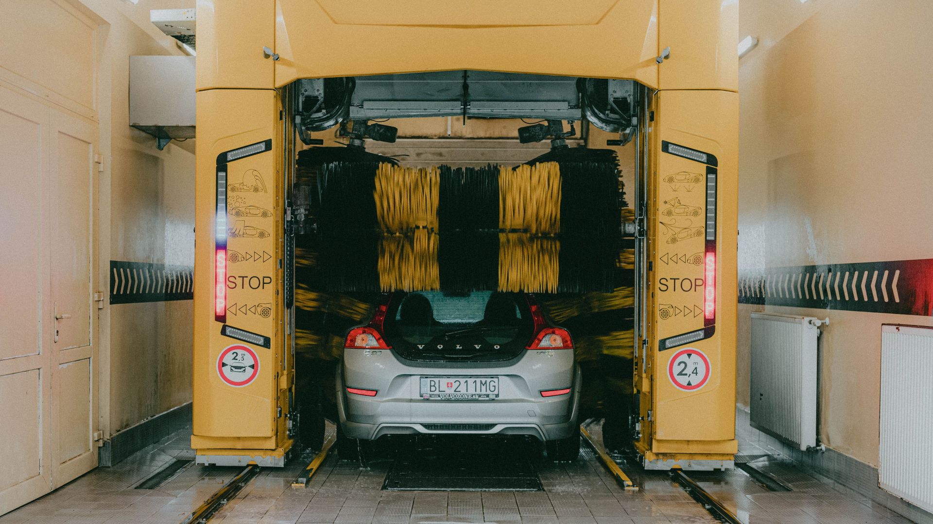 A car undergoing a cleaning process in an automated car wash station with a yellow gantry machine.