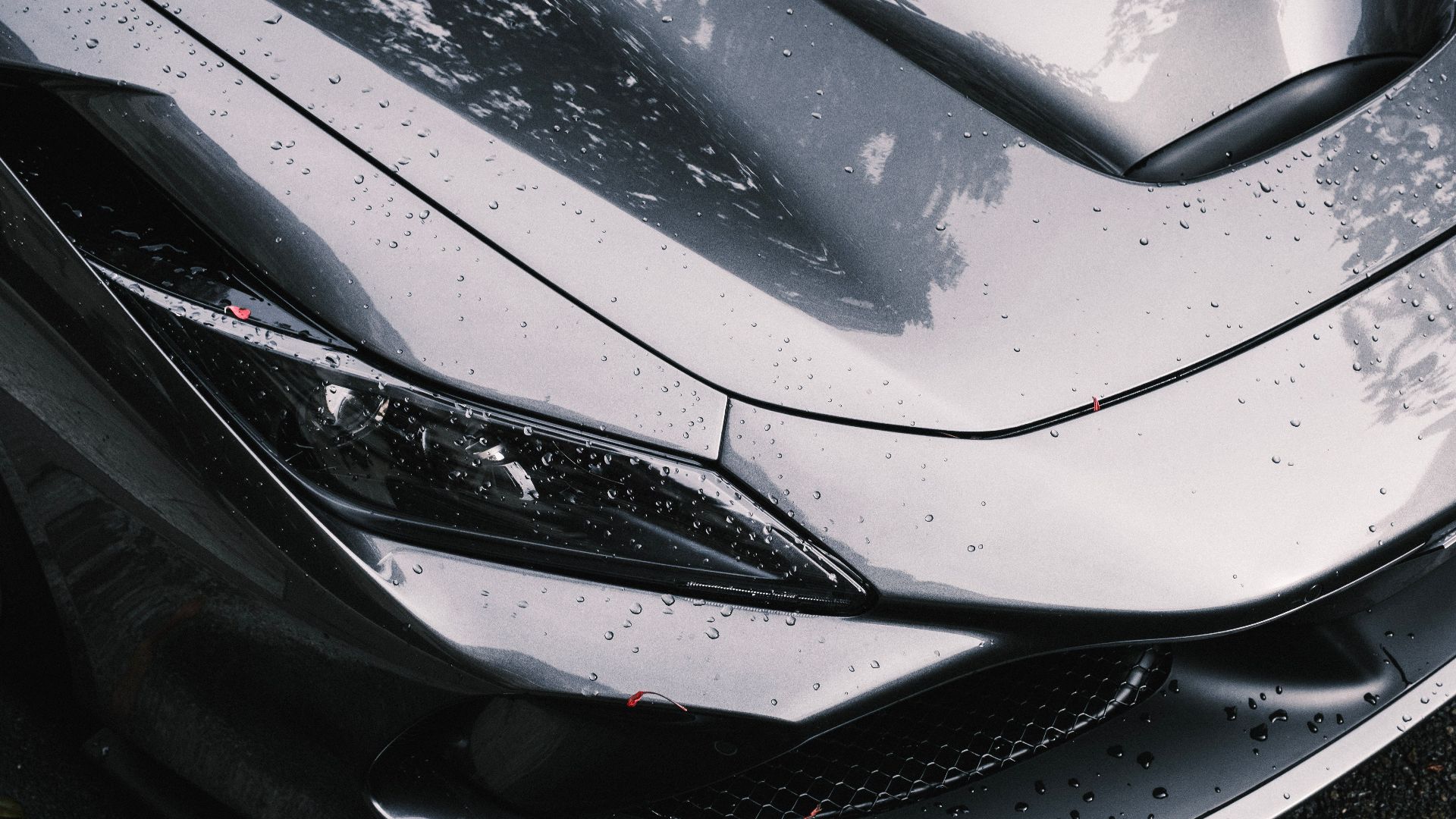 Detailed view of a luxury silver car with raindrops, highlighting sleek design and headlight features.
