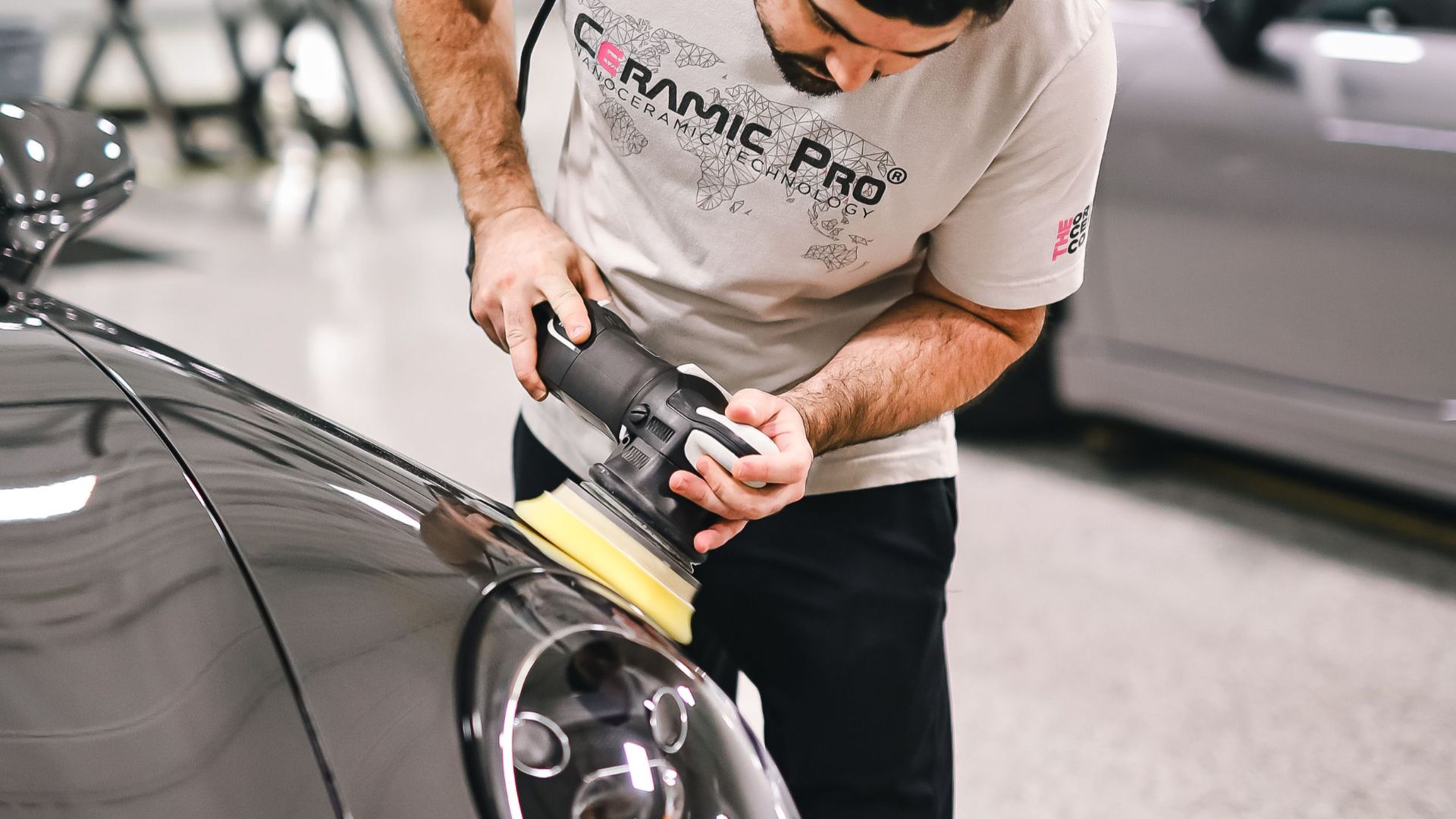 Man polishing a car's hood with precision in a modern automotive workshop.