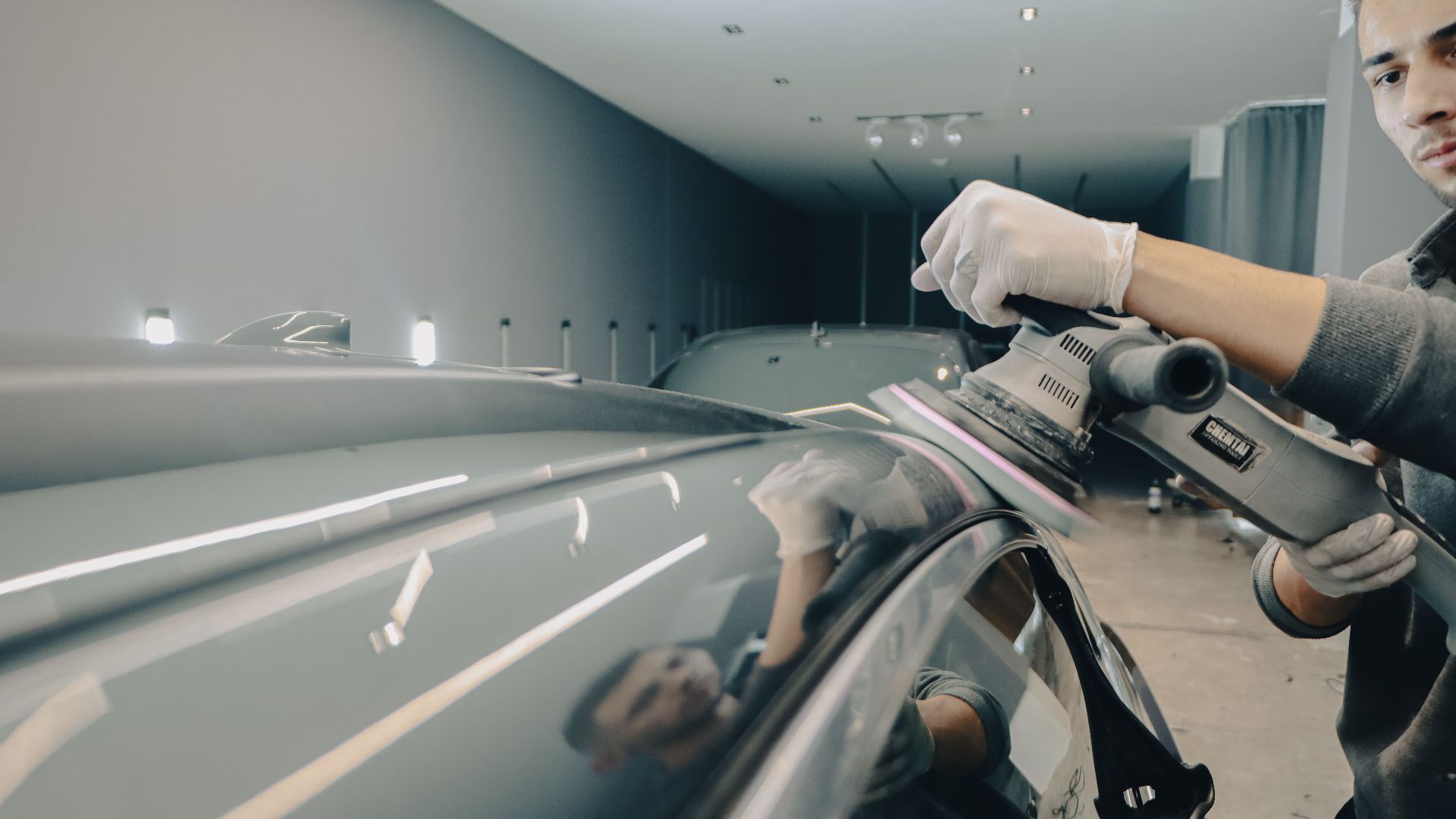 Worker using electric polisher on car roof for a shiny finish in an auto workshop.