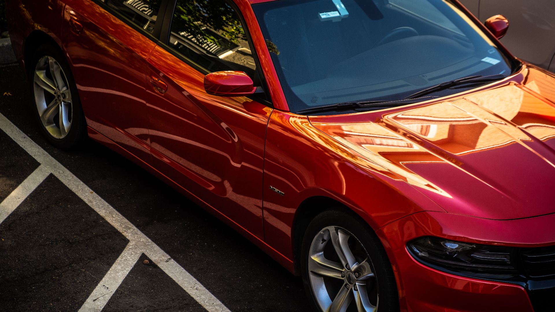 Red car parked diagonally in urban parking lot with sunlit reflections on sleek surface.