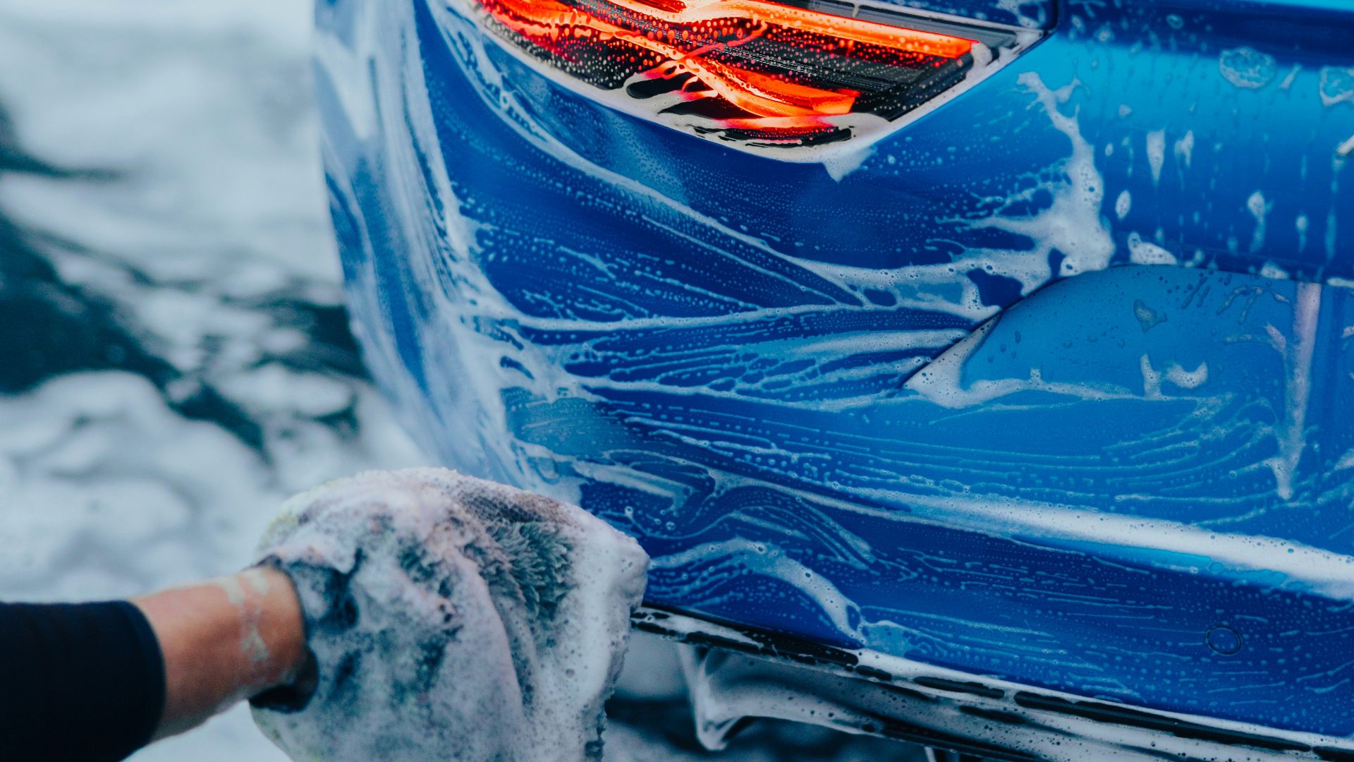 a person washing a blue car with a rag