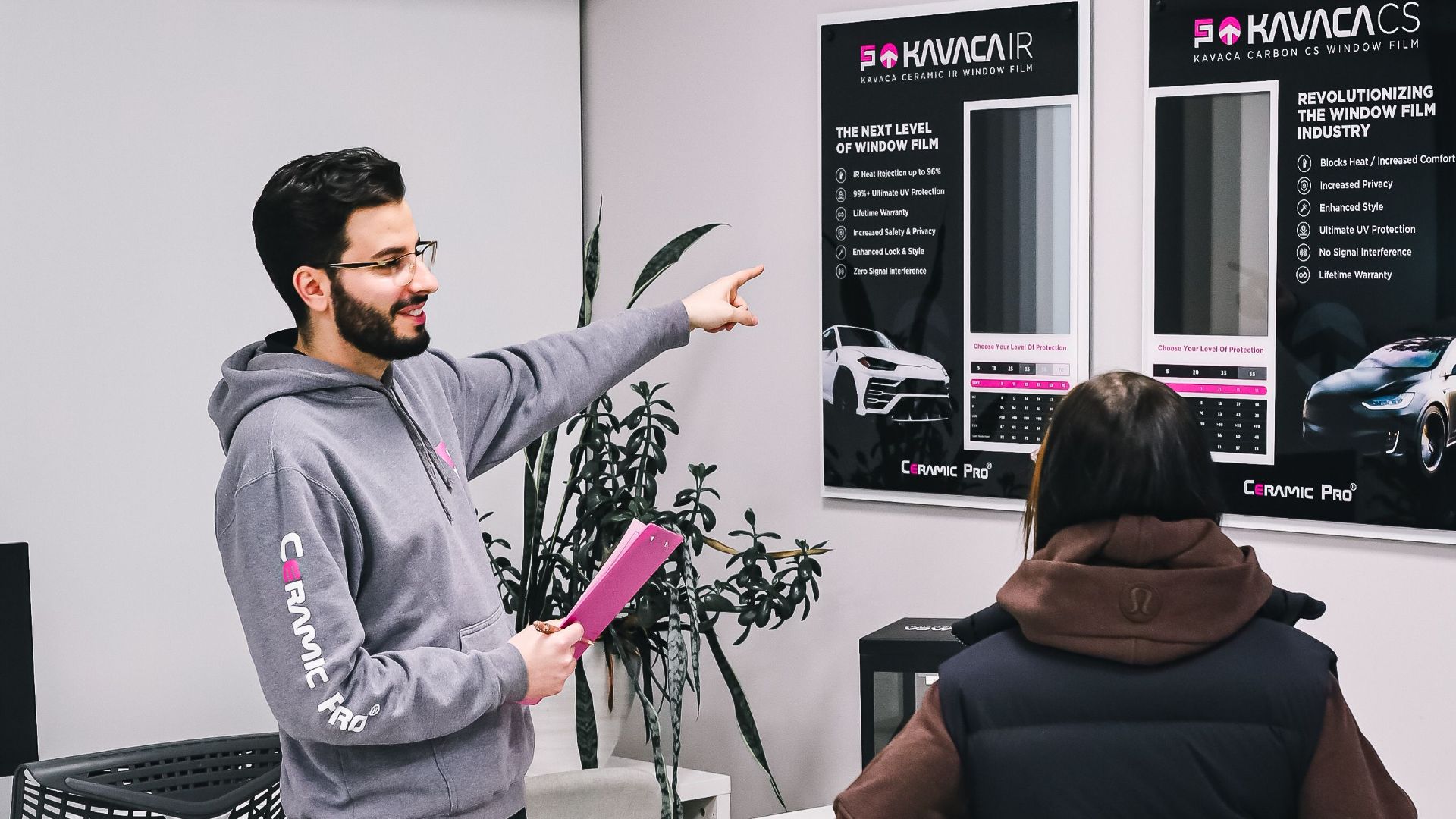A man assisting a customer in a car showroom with product options.