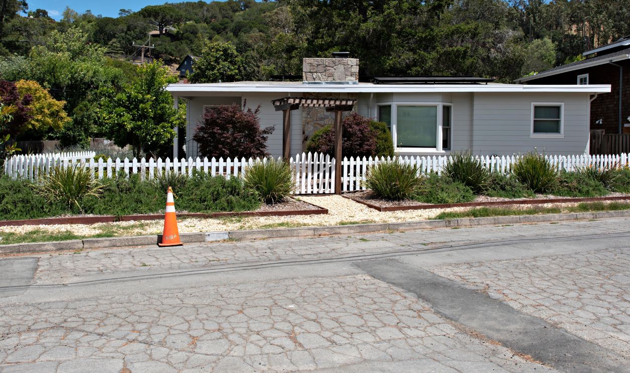 Cracked Asphalt and an Orange Cone in Front of a One-Story Suburban House