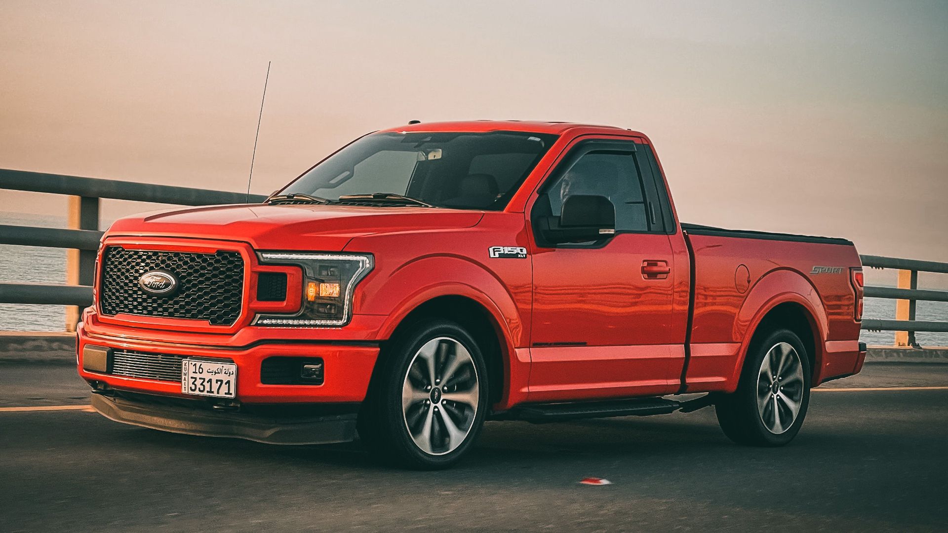 Red Ford F-150 truck driving on a bridge during sunset. Sleek and modern vehicle on the move.