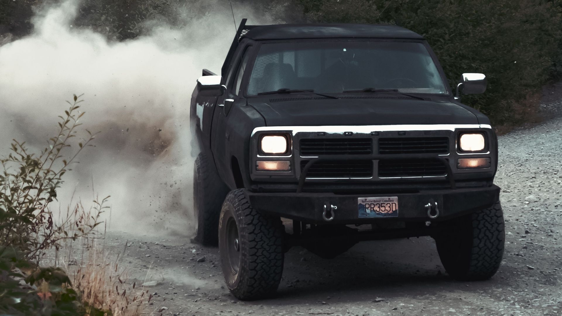 A rugged truck driving fast on a dirt road, surrounded by dust and greenery.