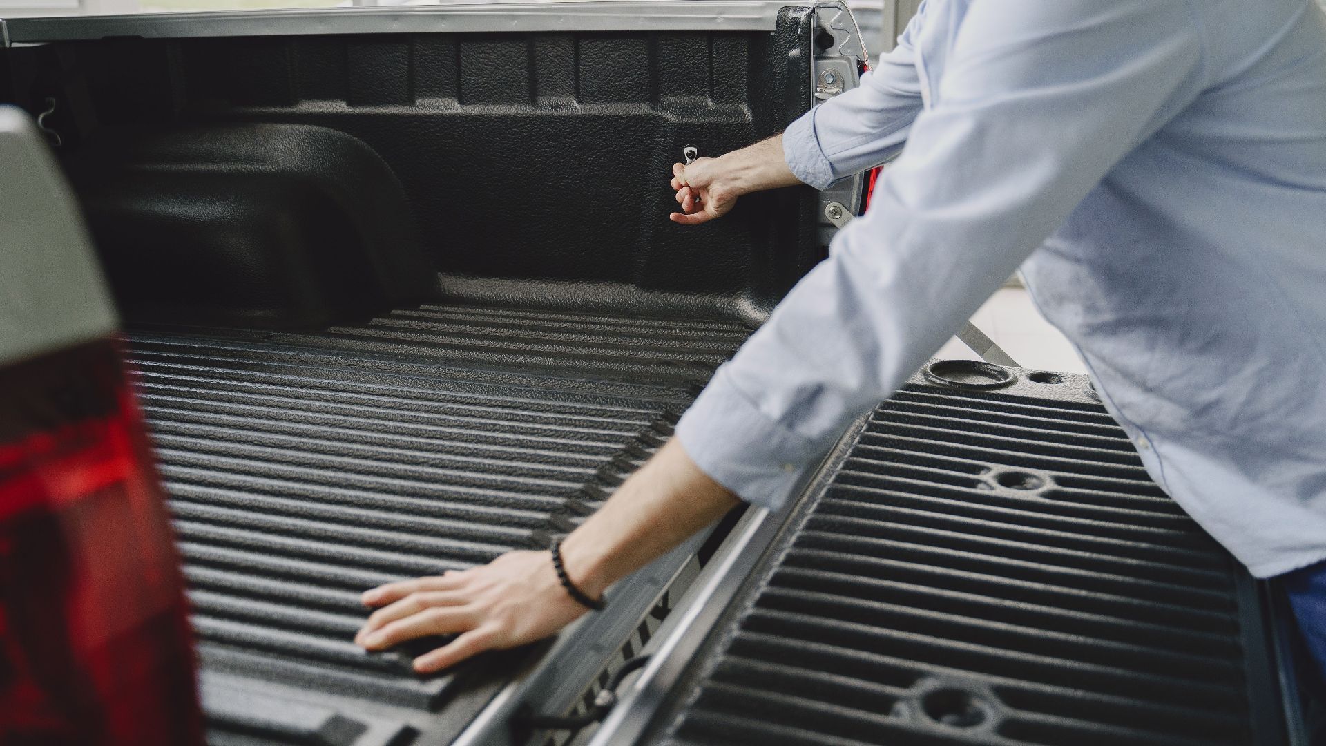 A man in a blue shirt opens the bed of a truck in a brightly lit indoor space.