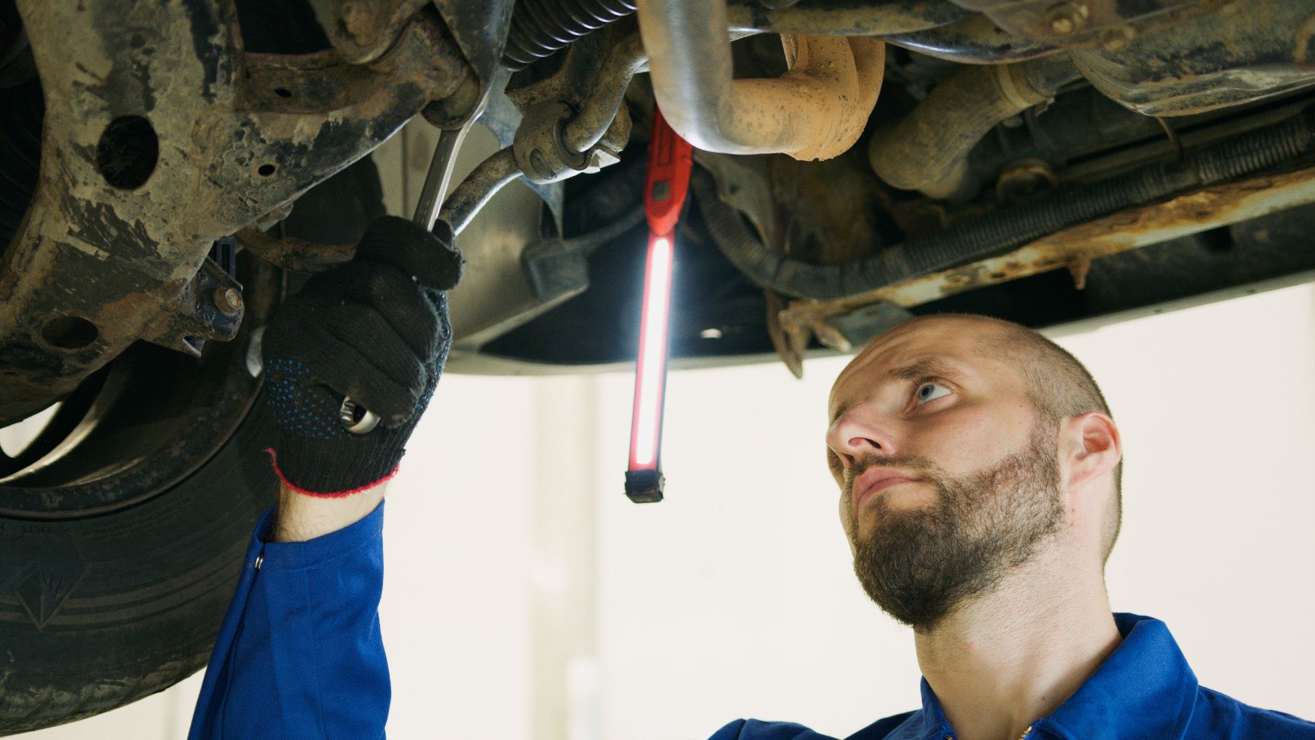 Mechanic focusing on vehicle maintenance under a car lift in a garage.
