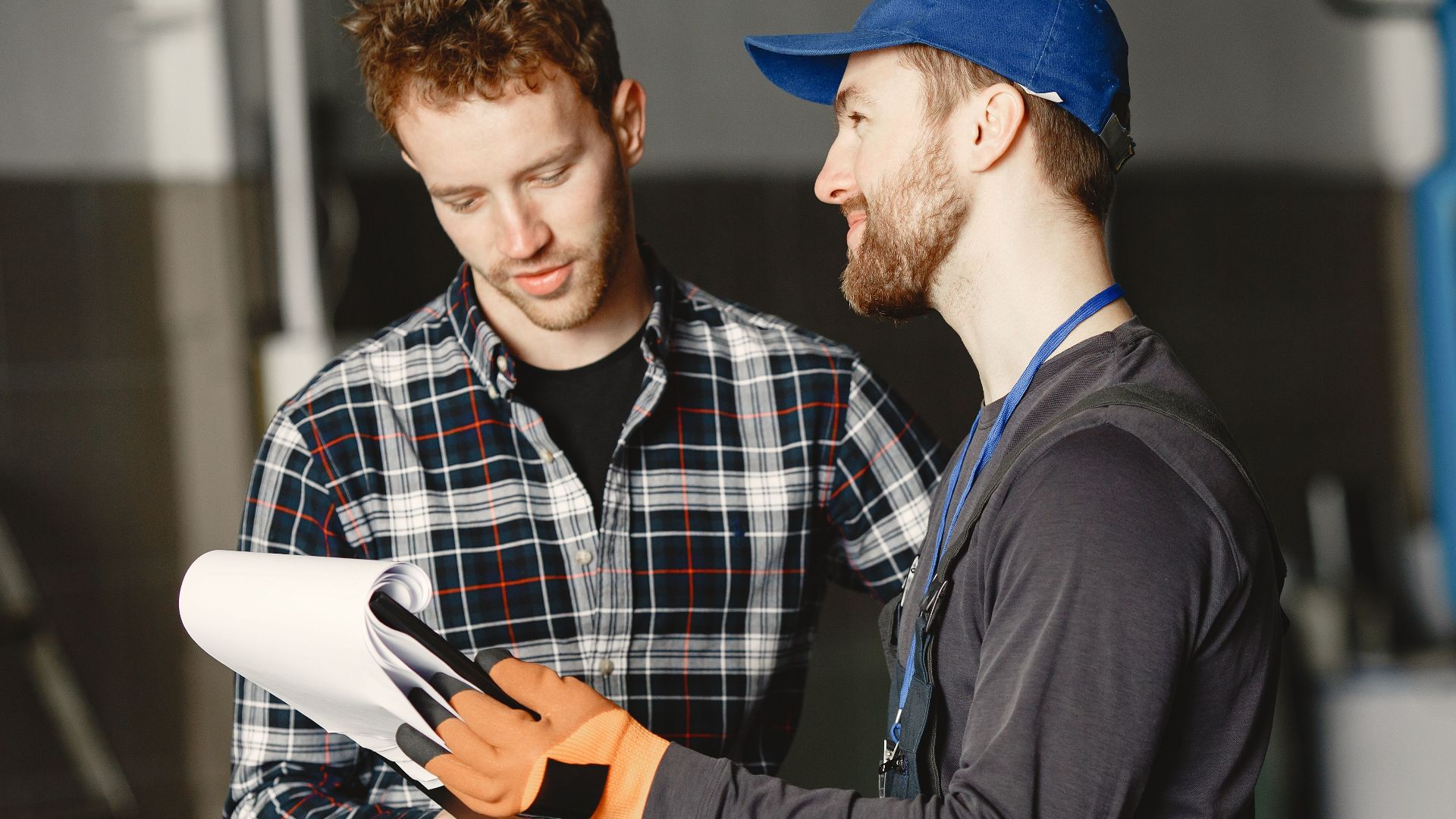 Mechanic in uniform consults with customer in garage setting beside a blue truck.