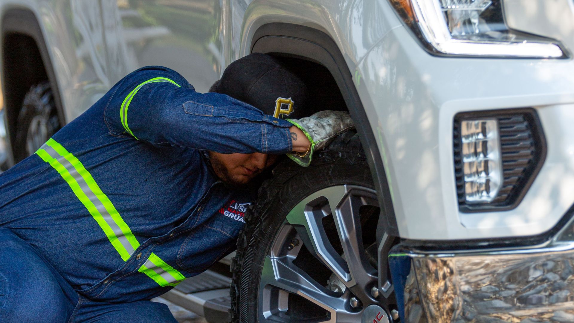 Mechanic working on the wheel of a white off-road vehicle outdoors, fixing a problem.