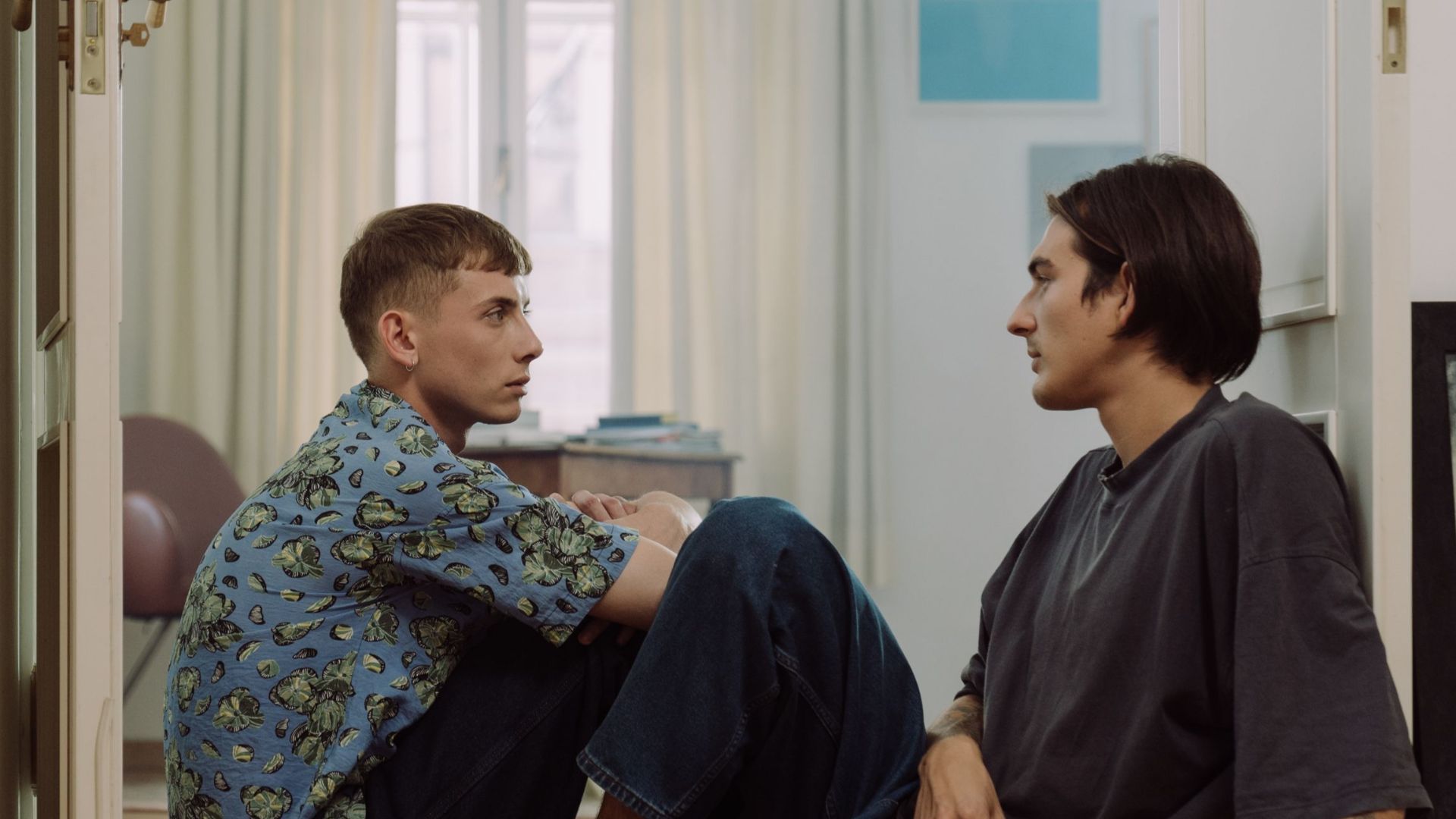 Two men sit together in a cozy room, sharing a deep conversation and a glass of wine.