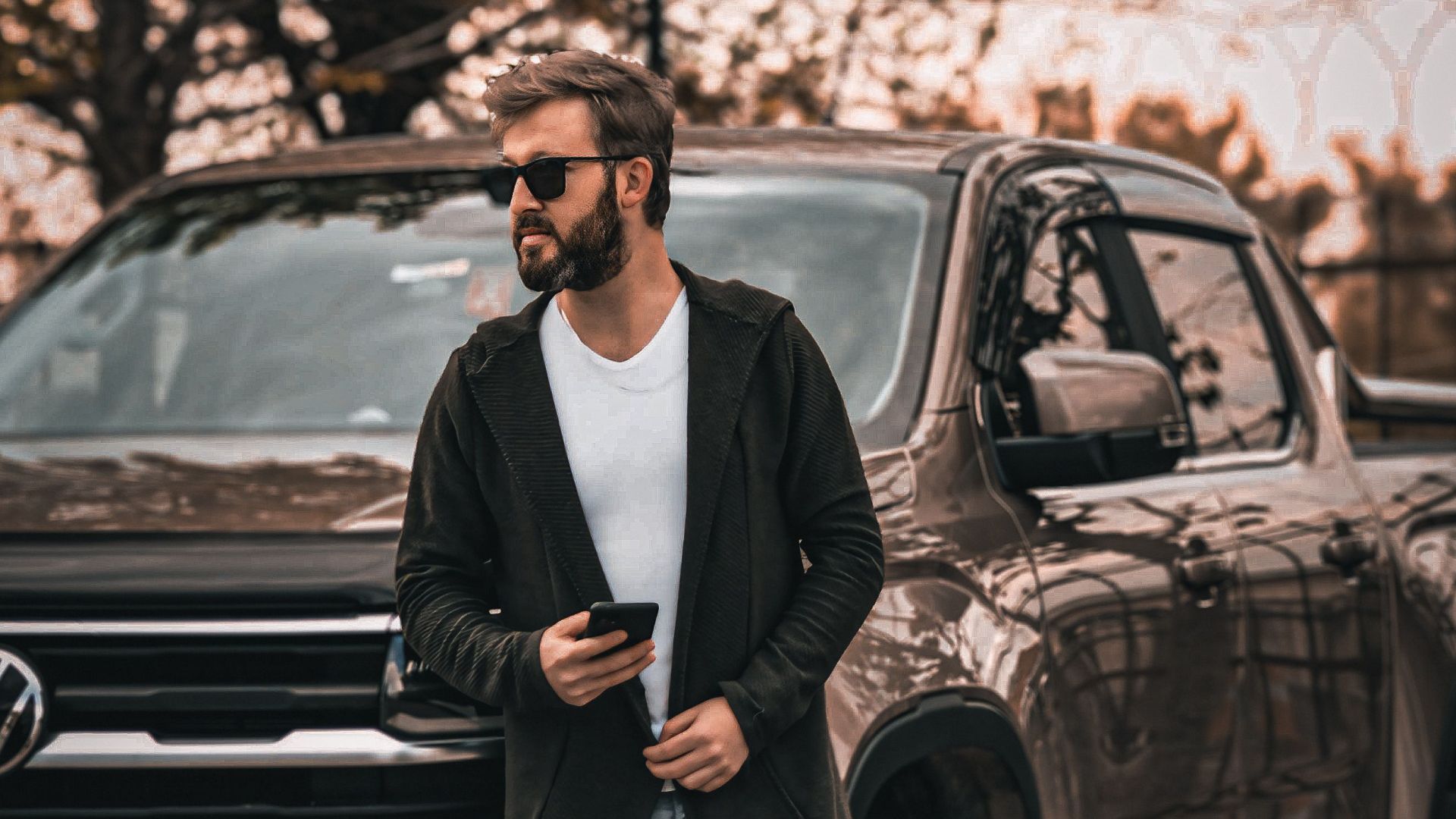 Stylish man with sunglasses and smartphone leaning against a Volkswagen pickup truck outdoors.