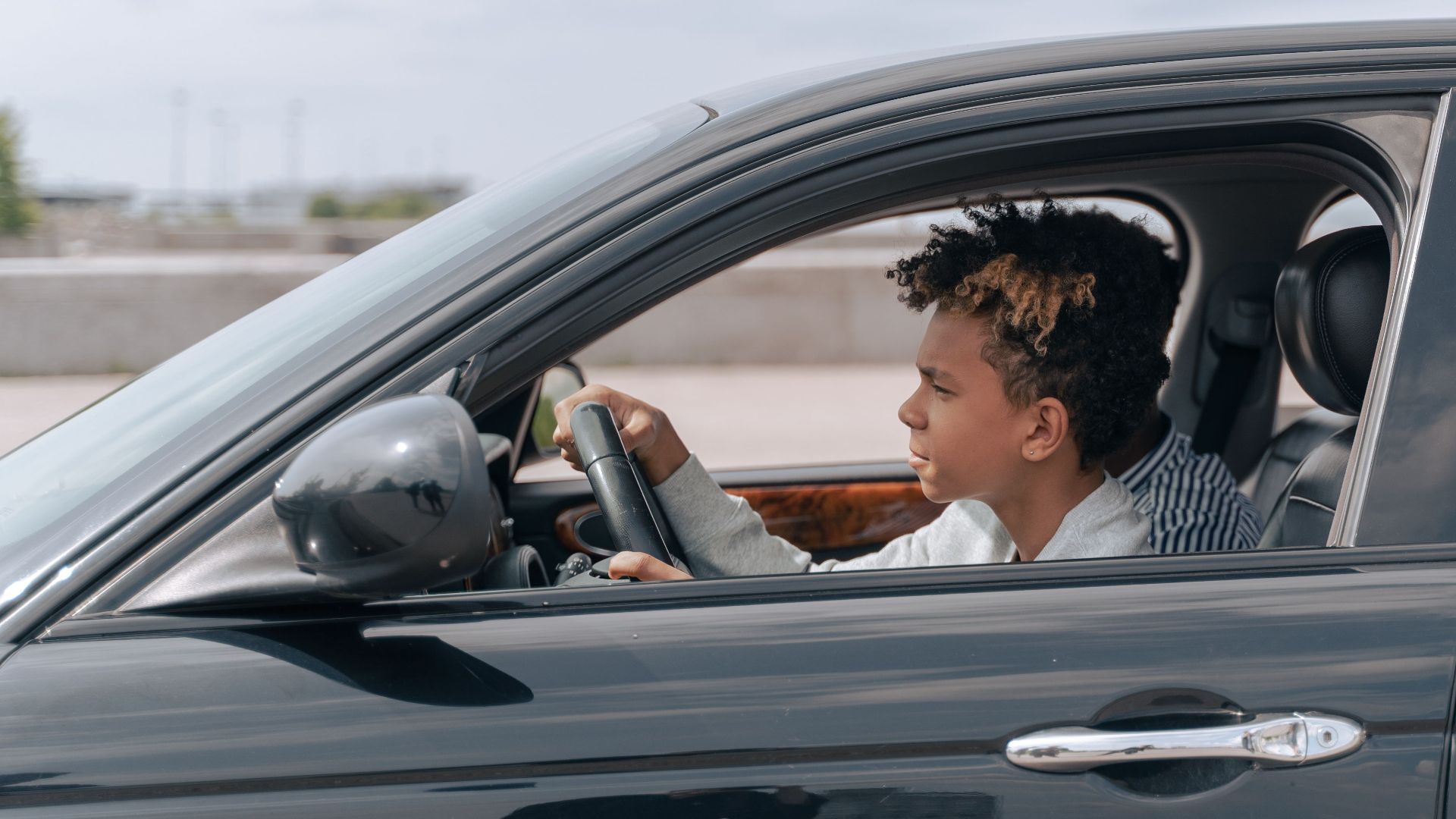 Side view of a young male teenager focused on driving a car in bright daylight.